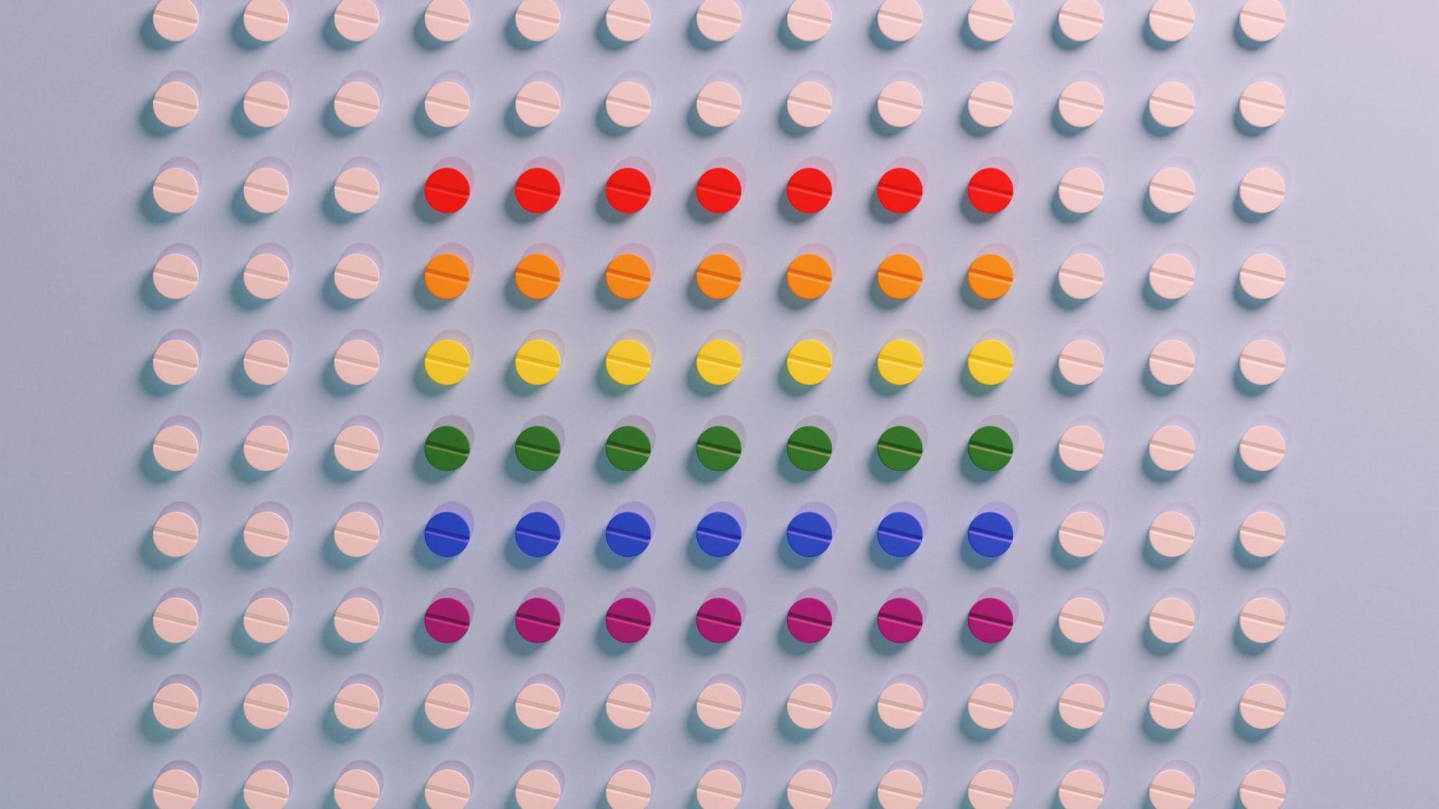 Collums of white pills sit on a blue backround. There are 10 rows, with 13 pills in each row. In the centre of these pills there are muti-coloured ones. Each row is a different colour, from top to bottom they're red, orange, yellow, green, blue and purple.