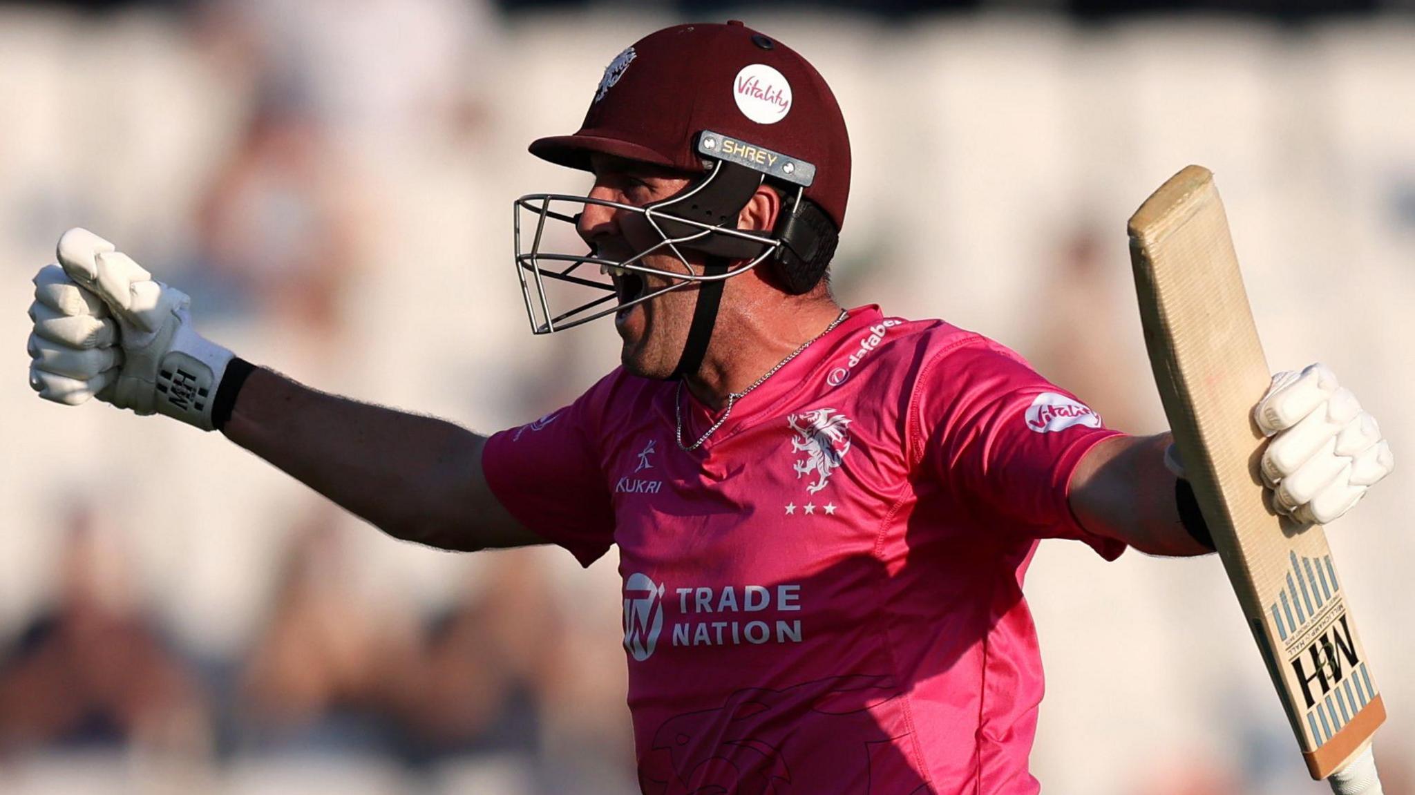 Craig Overton, wearing Somerset's pink shirt, celebrates the win over Yorkshire by shouting and punching his fists out while holding his bat in his left hand.