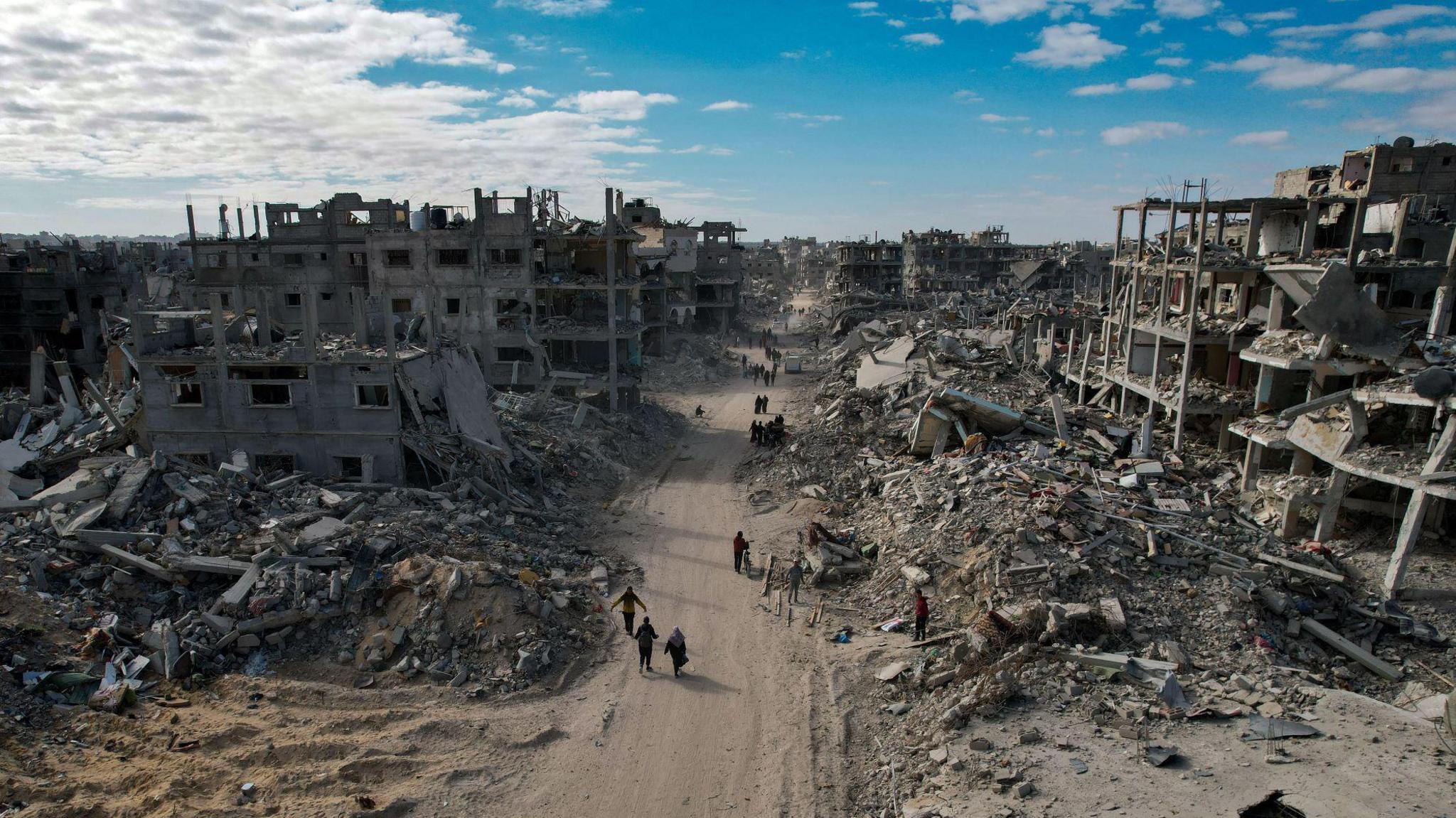 An aerial view taken with a drone shows internally displaced Palestinians walking along a street among the grey, dusty rubble of destroyed buildings in Rafah 