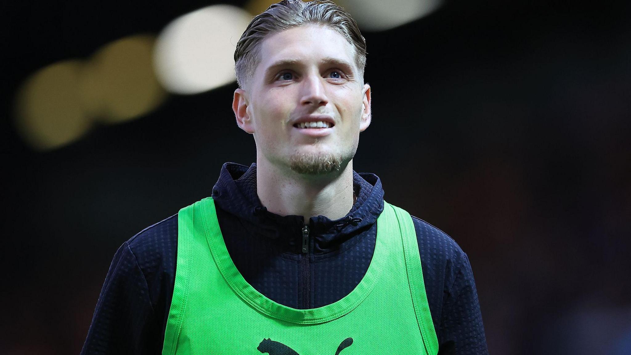 Plymouth Argyle defender Kornel Szucs, wearing a green bib and navy blue hoodie, warms up before a match