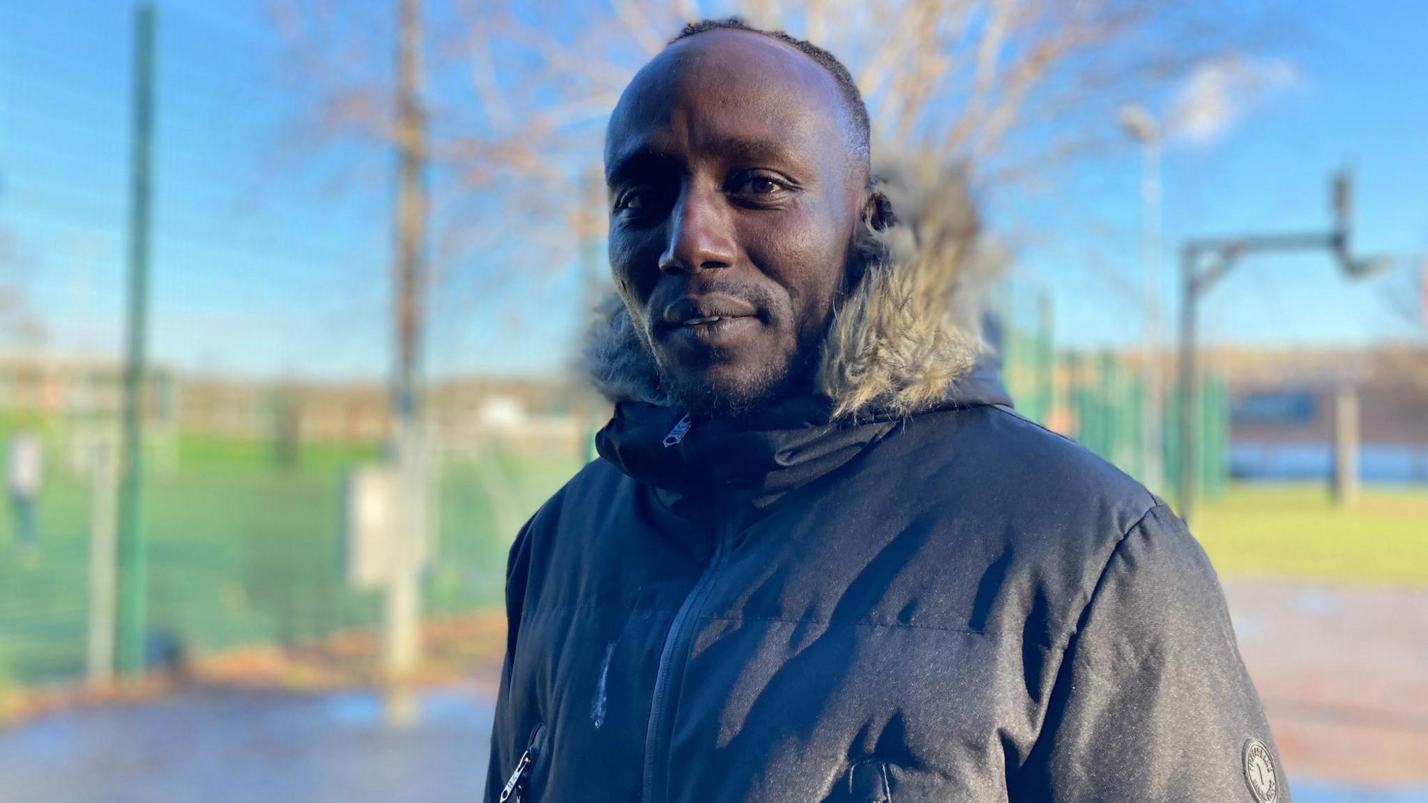 Derrick wearing a large winter coat and furry collar looks towards the camera.