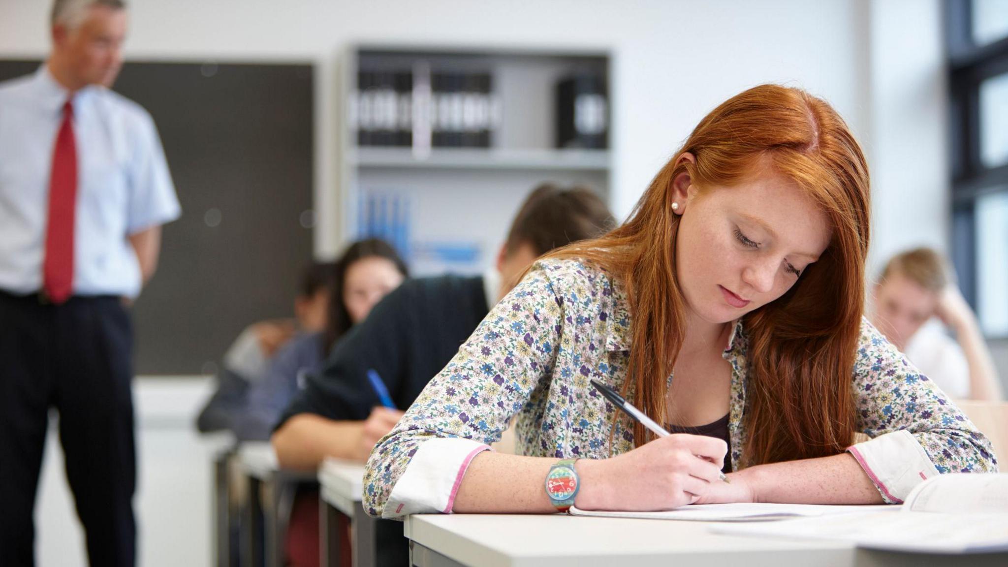 A teacher watching over teenagers in a classroom.