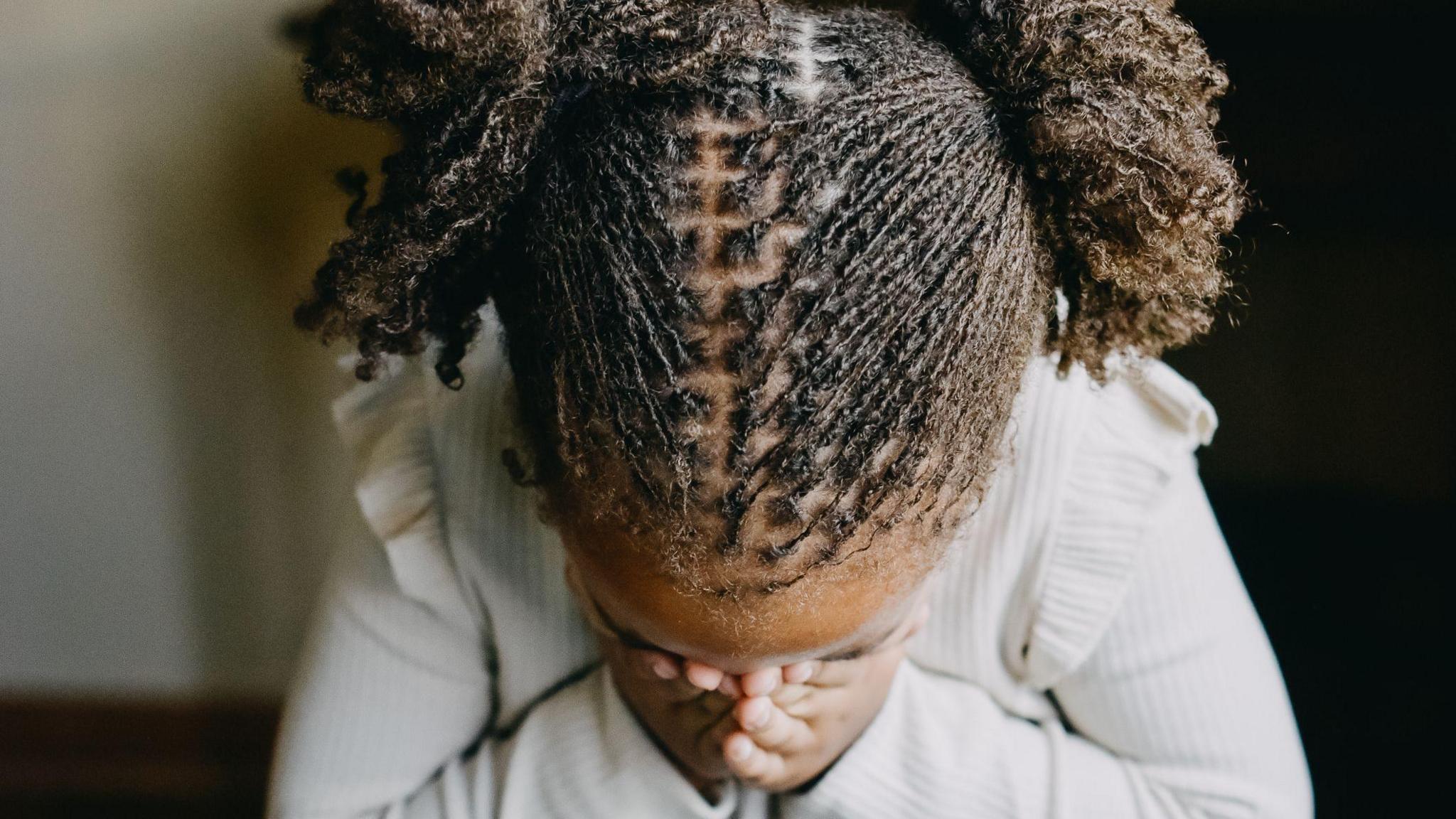A girl has her head in her hands. She is wearing a white shirt and has her hair in two buns. 