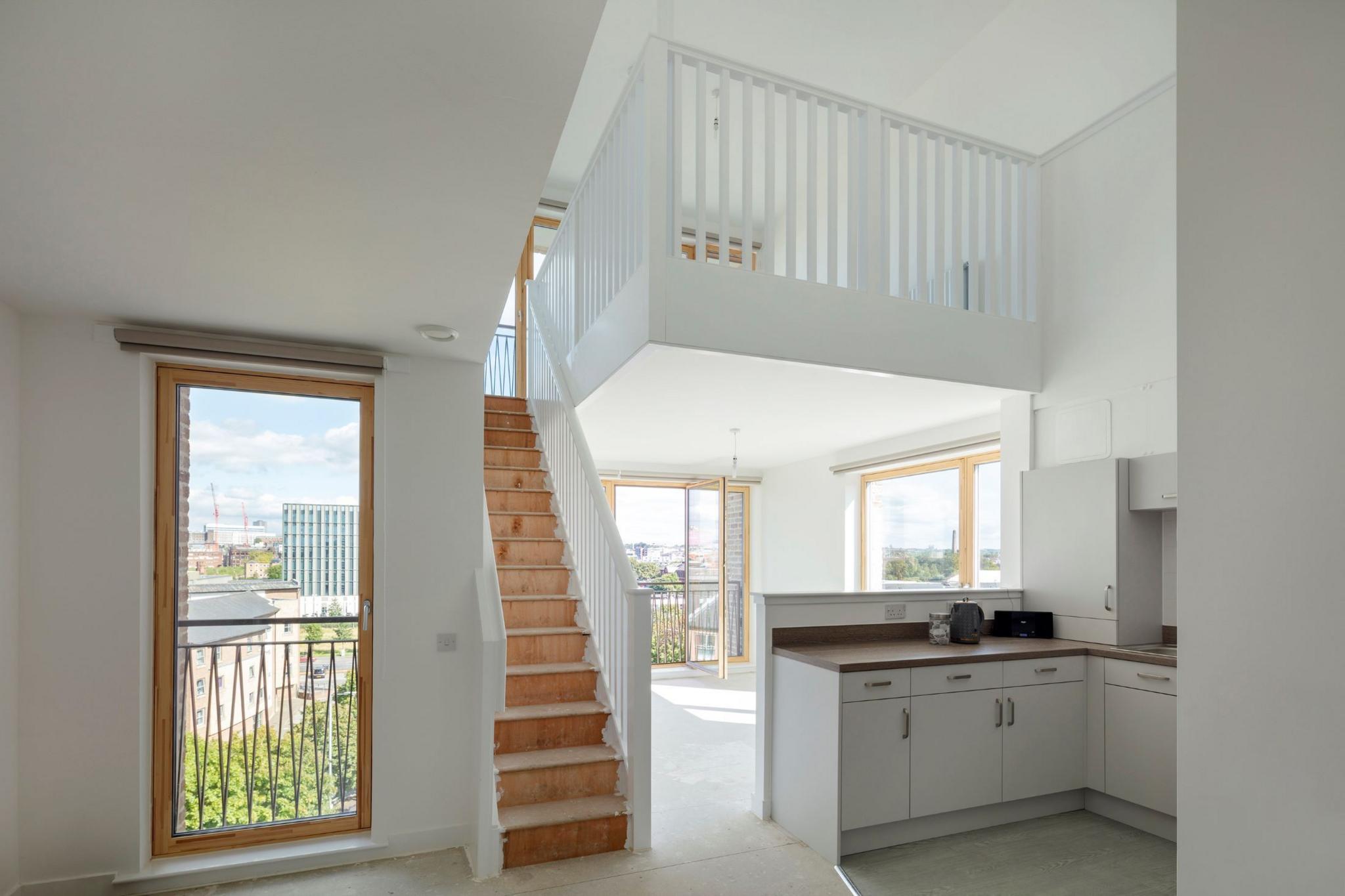 Apartment with a white staircase to a mezzanine level. There are windows on every wall letting loads of light in