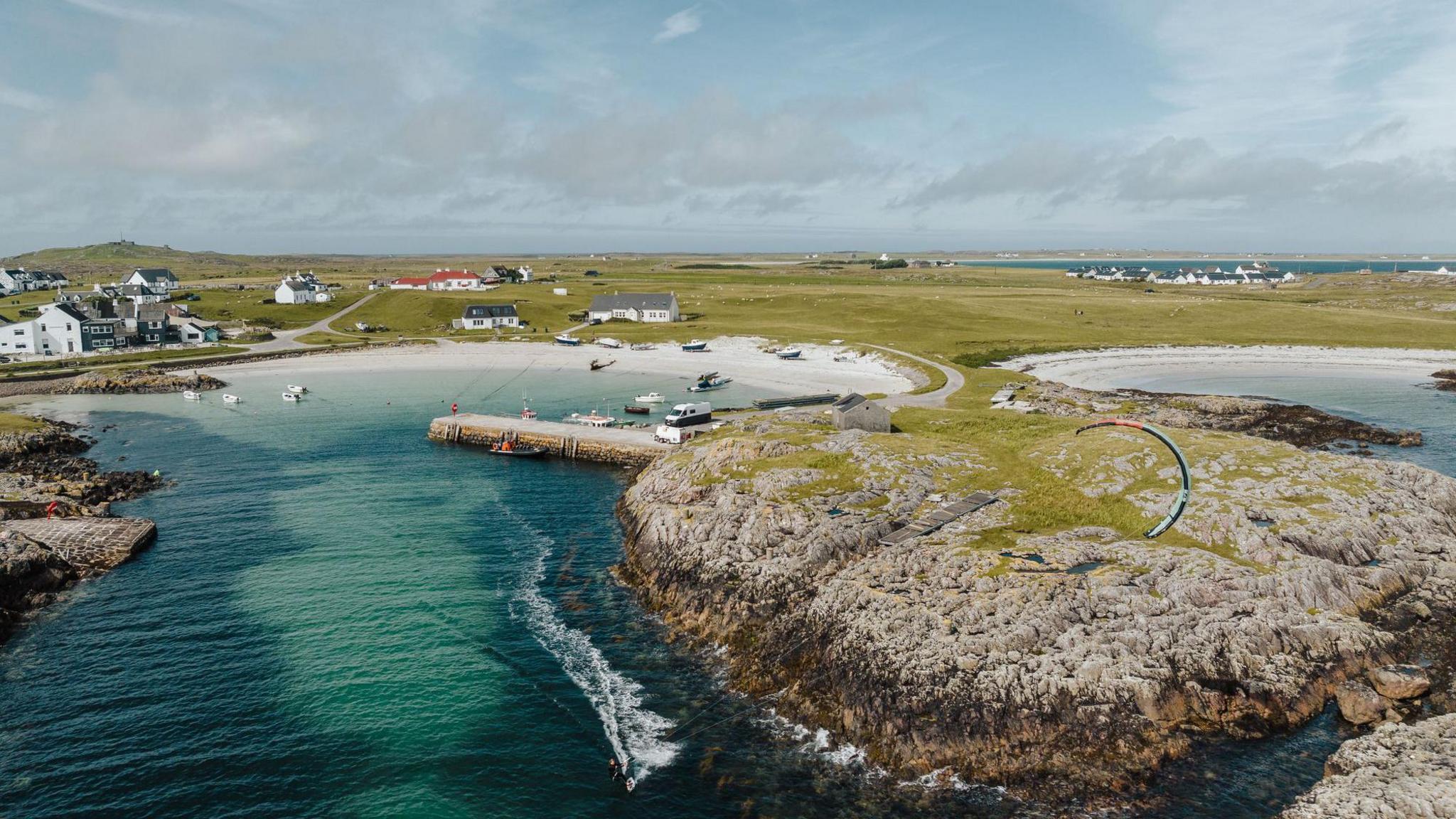 White sandy beaches of Tiree. Clear blue waters. A smattering of white buildings and a large expanse of green fields. 