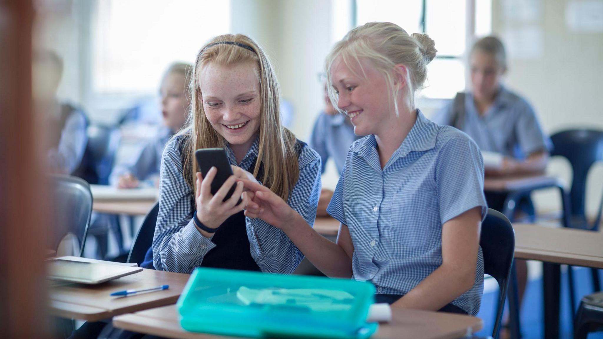 Two girls looking at mobile phone in classroom. 