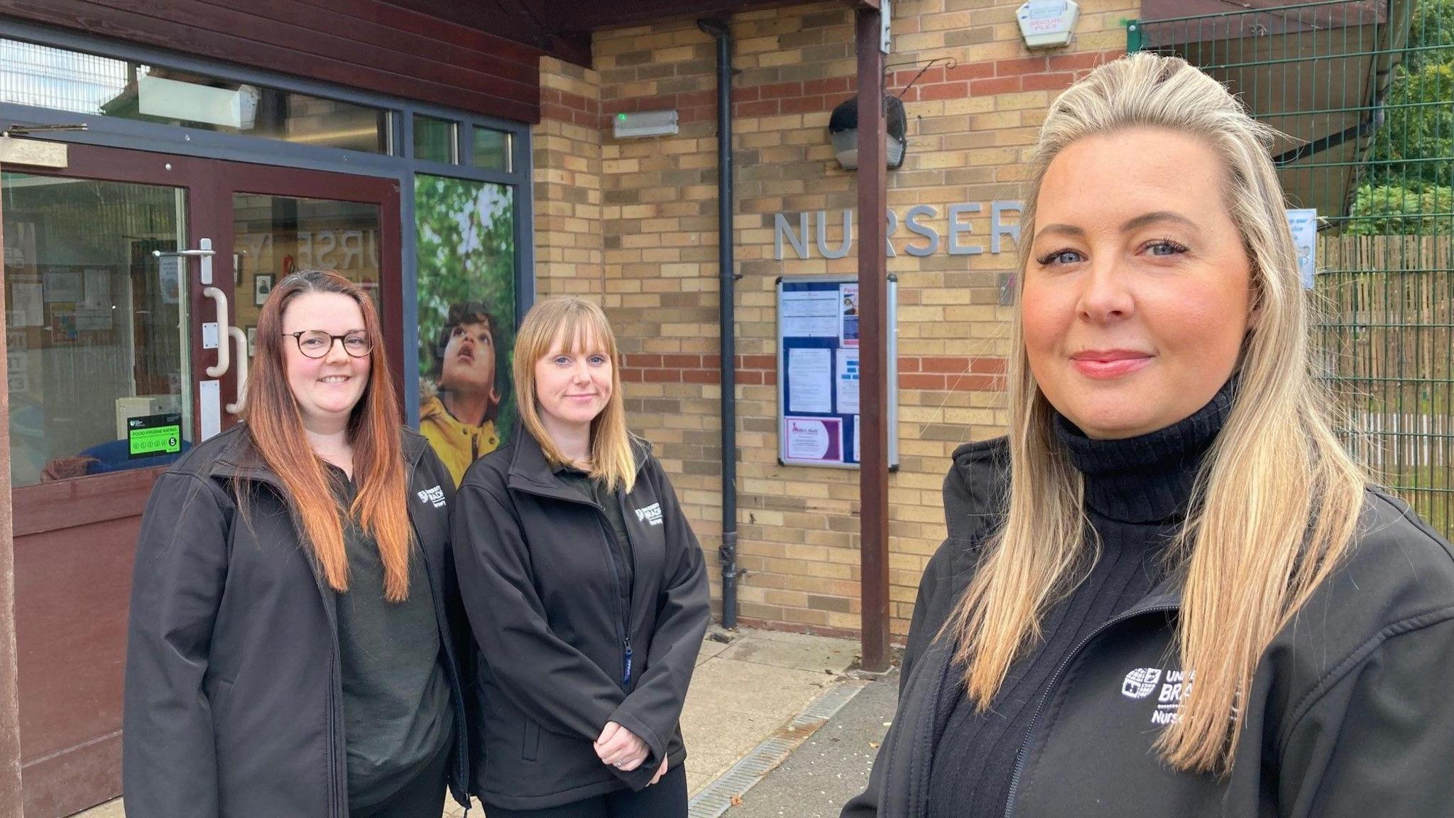 Three women wearing matching black jackets with white logos on them spelling out The University of Bradford 