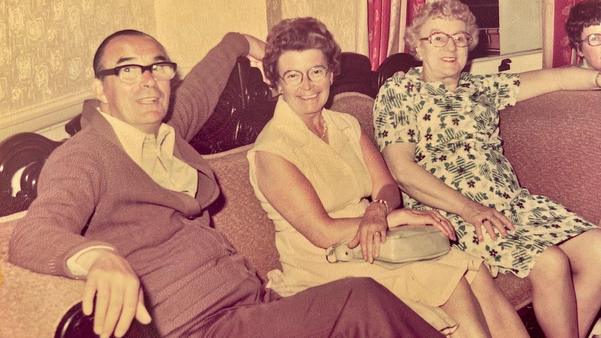 Jim and Isobel Rankin (middle) smiling at the camera as they sit on a sofa with others in bed and breakfast accommodation