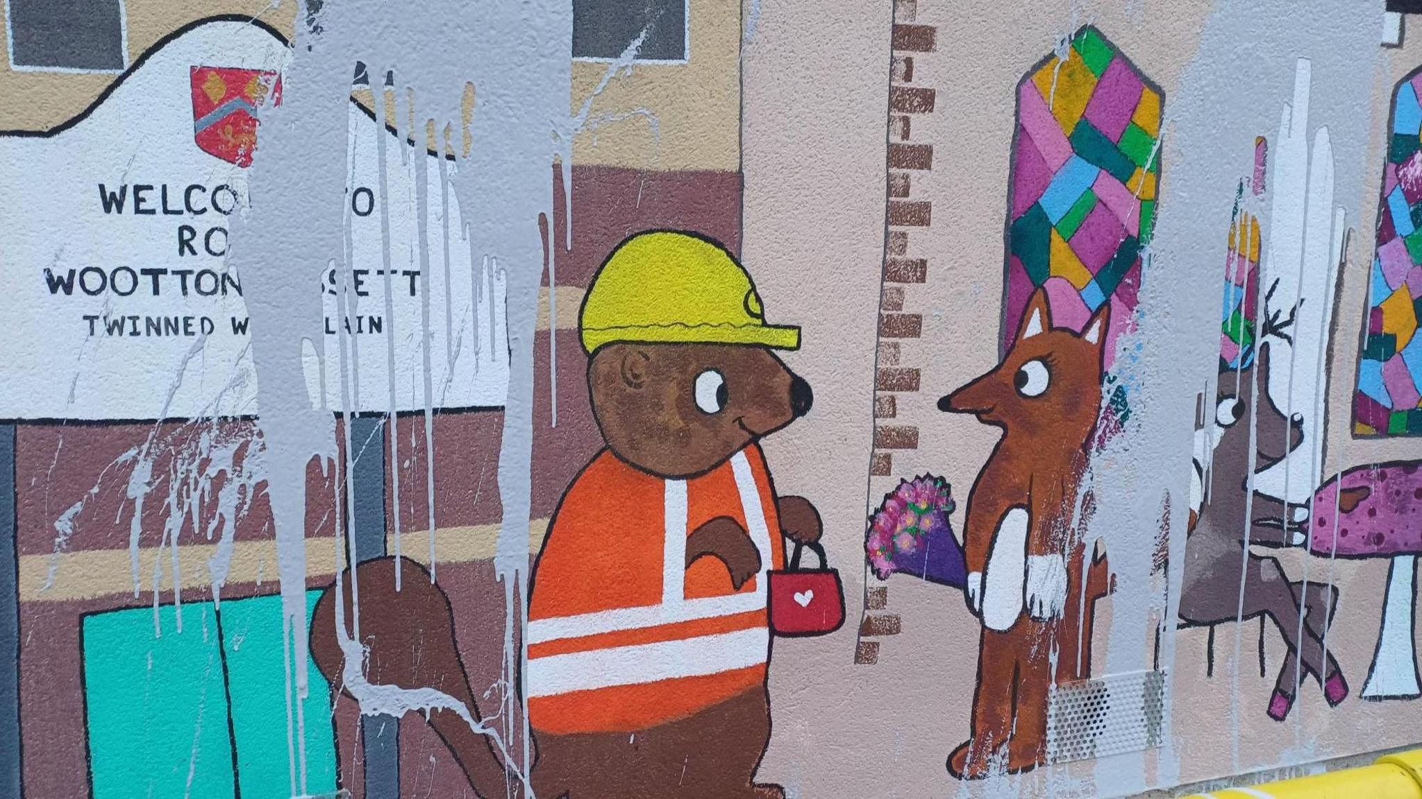 A mural featuring smiling cartoon woodland creatures, including a squirrel in a high-vis vest and hard hat and a fox carrying a bouquet of flowers. The mural has been splashed with light grey paint.