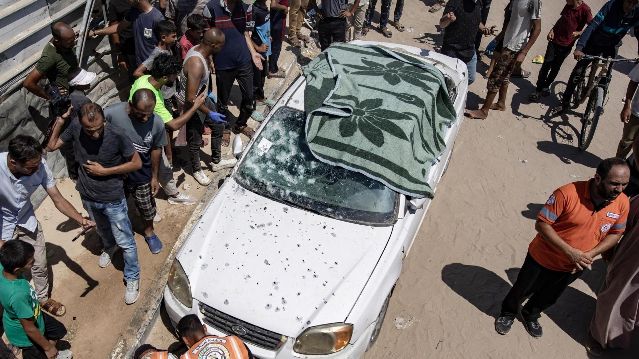 Palestinians inspect a car damaged in an Israeli air strike in al-Mawasi, southern Gaza (16 July 2024)