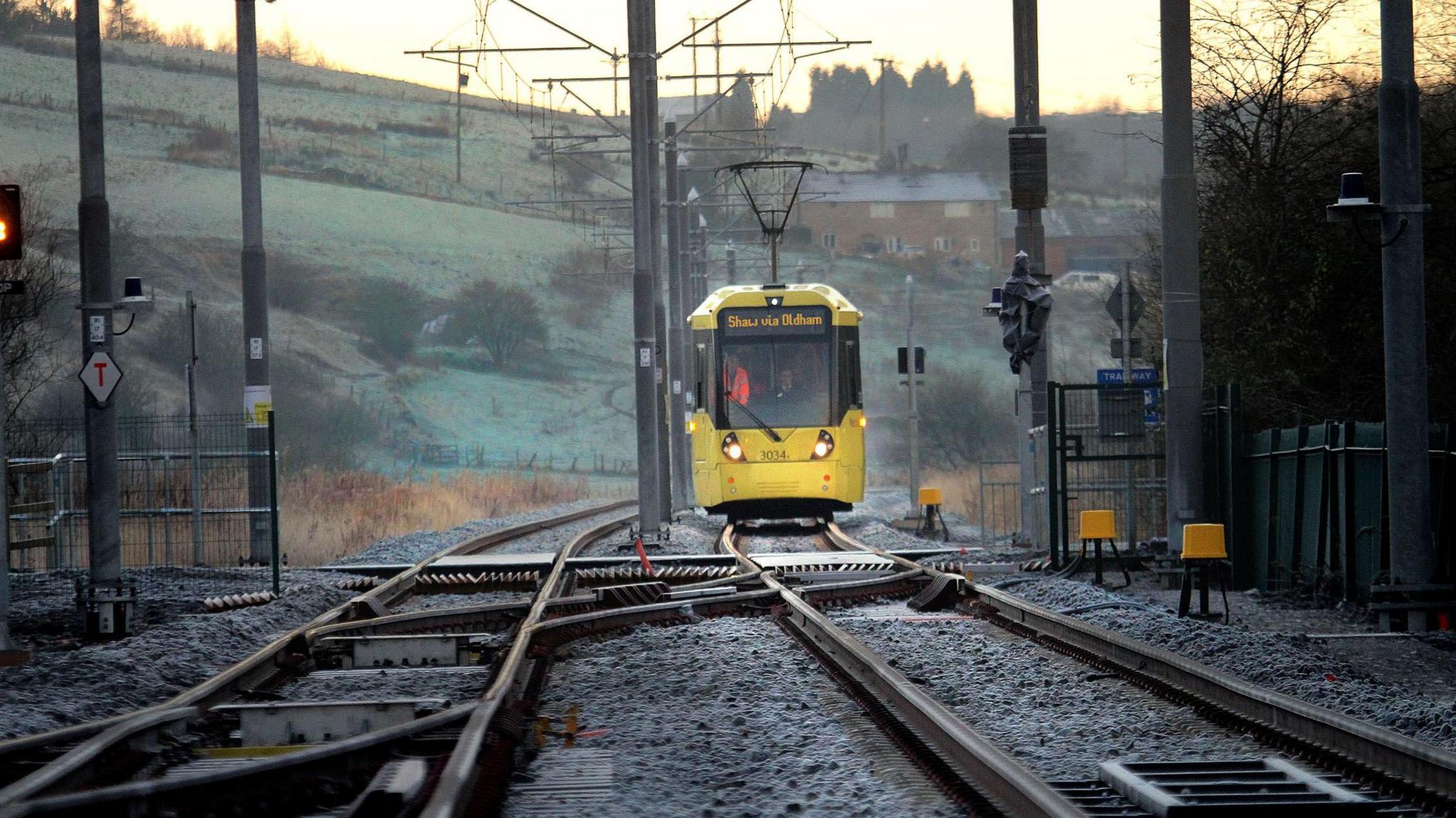 A yellow tram on a rural track. Foggy hills can be seen behind