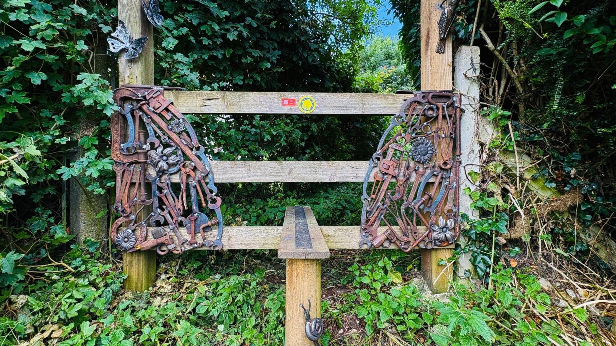 A stile through a hedge with recycled metal tools attached to each side