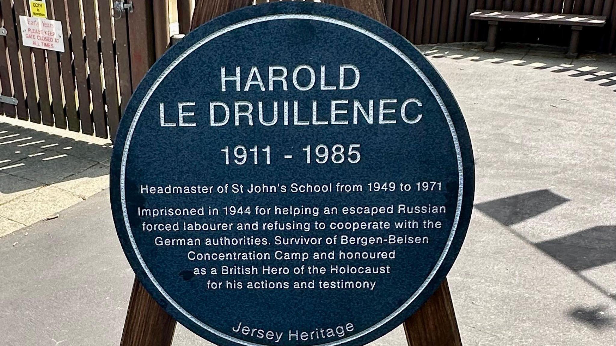 The plaque reads: "HAROLD LE DRUILLENEC 1911-1985 Headmaster of St John's School from 1949 to 1971. Imprisoned in 1944 for helping an escaped Russian forced labourer and refusing to cooperate with German authorities. Survivor of Bergen-Belsen Concentration Camp and honoured as a British Hero of the Holocaust for his actions and testimony. Jersey Heritage."