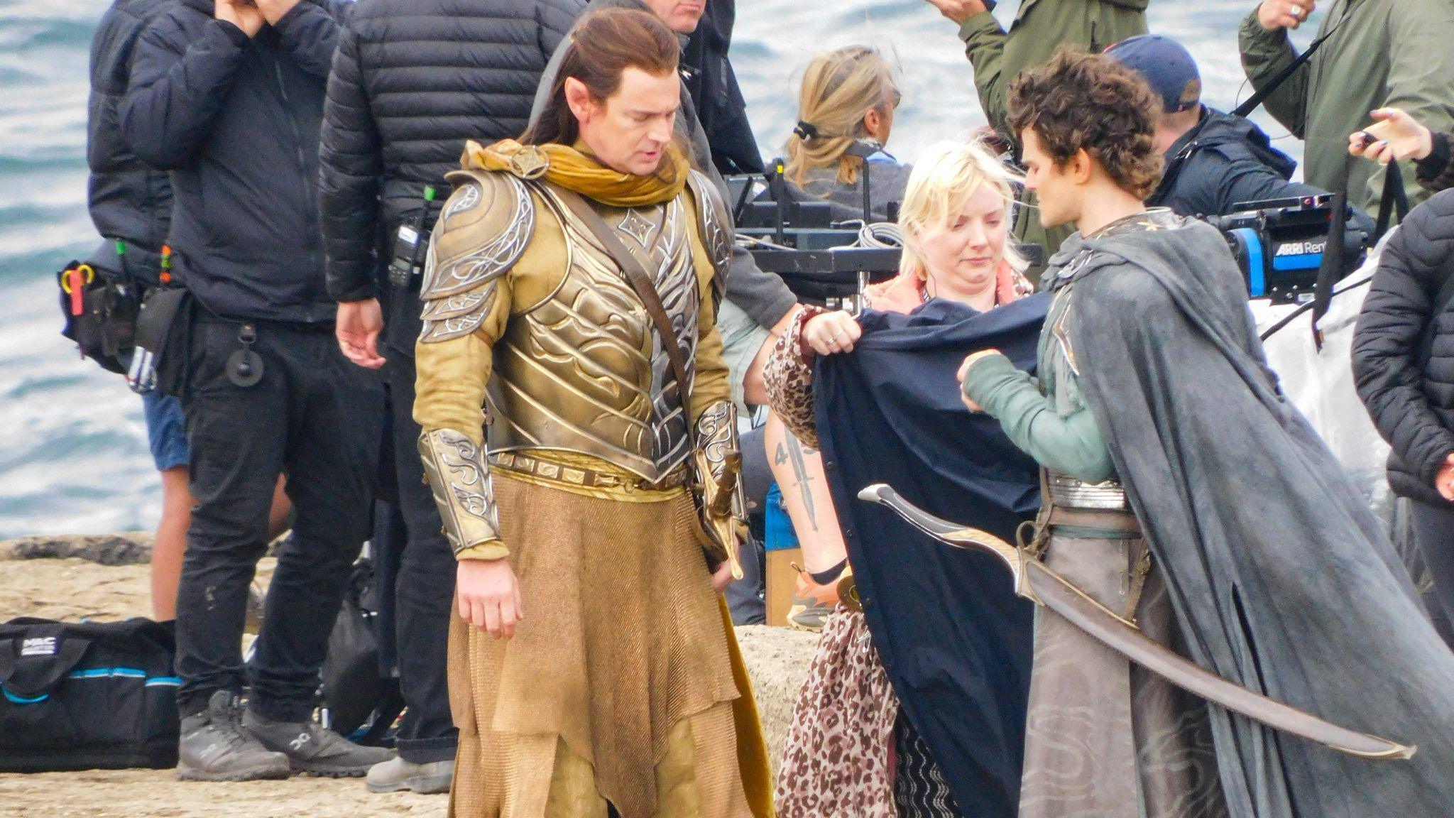 Actors Benjamin Walker, who plays the High King of the Elves Gil-Galad, and Robert Aramayo standing opposite each other as a member of the filming crew is handling what appears to be a piece of cloth near them. They are all looking down. Other members of the filming crew could be seen working behind him.