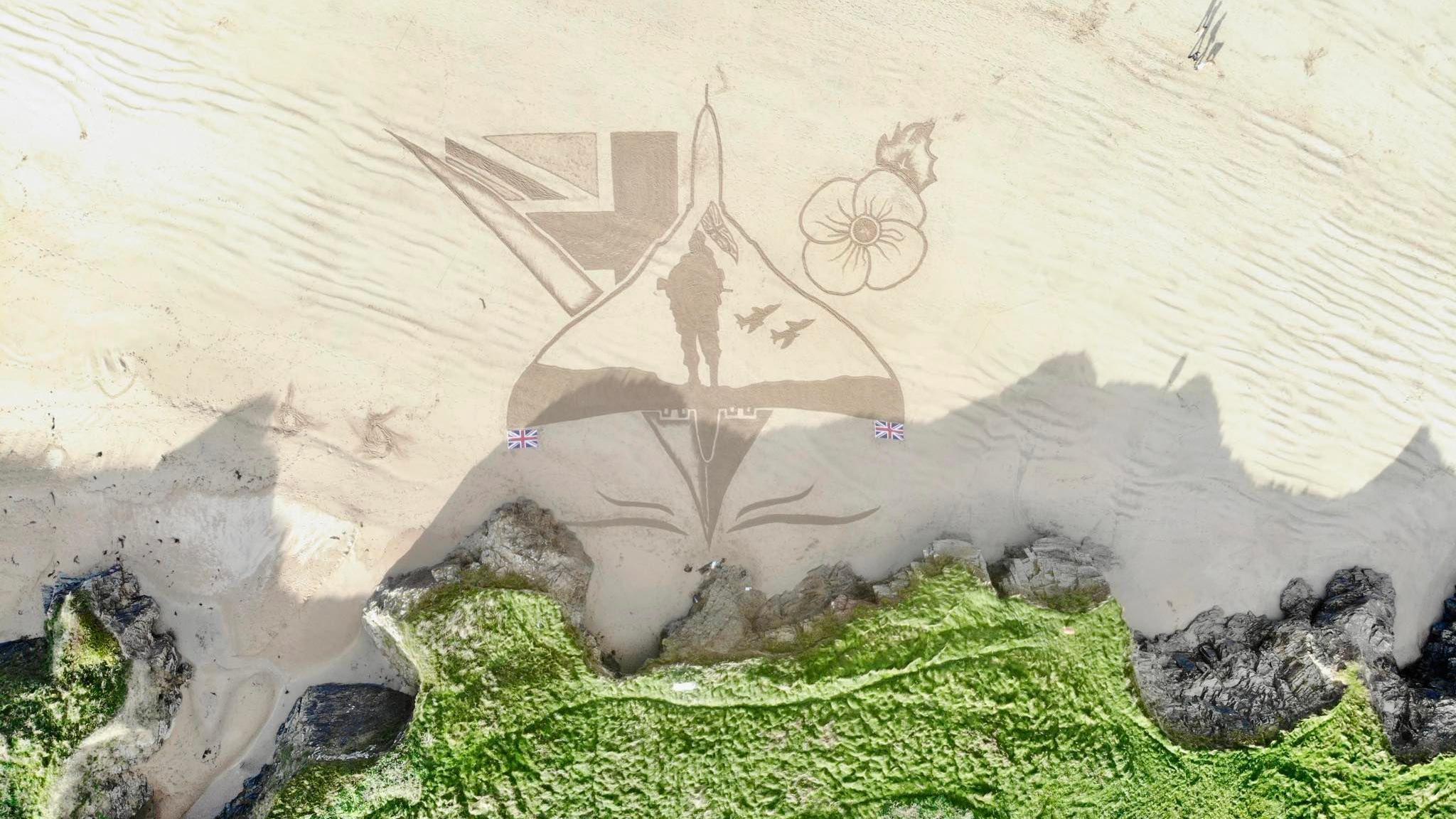 Overhead photo showing sand art of a Vulcan aircraft with a poppy, a soldier and union lags
