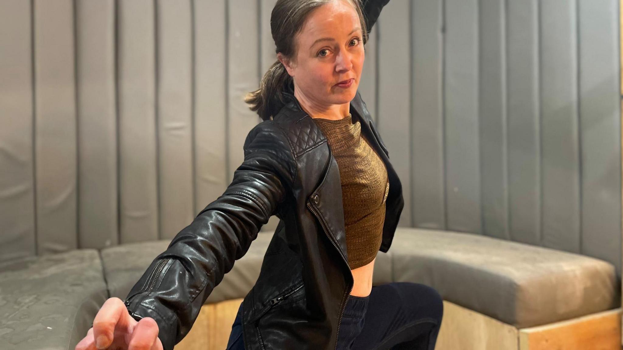 A woman in a black leather jacket kneels with her hand extended in a fight pose.