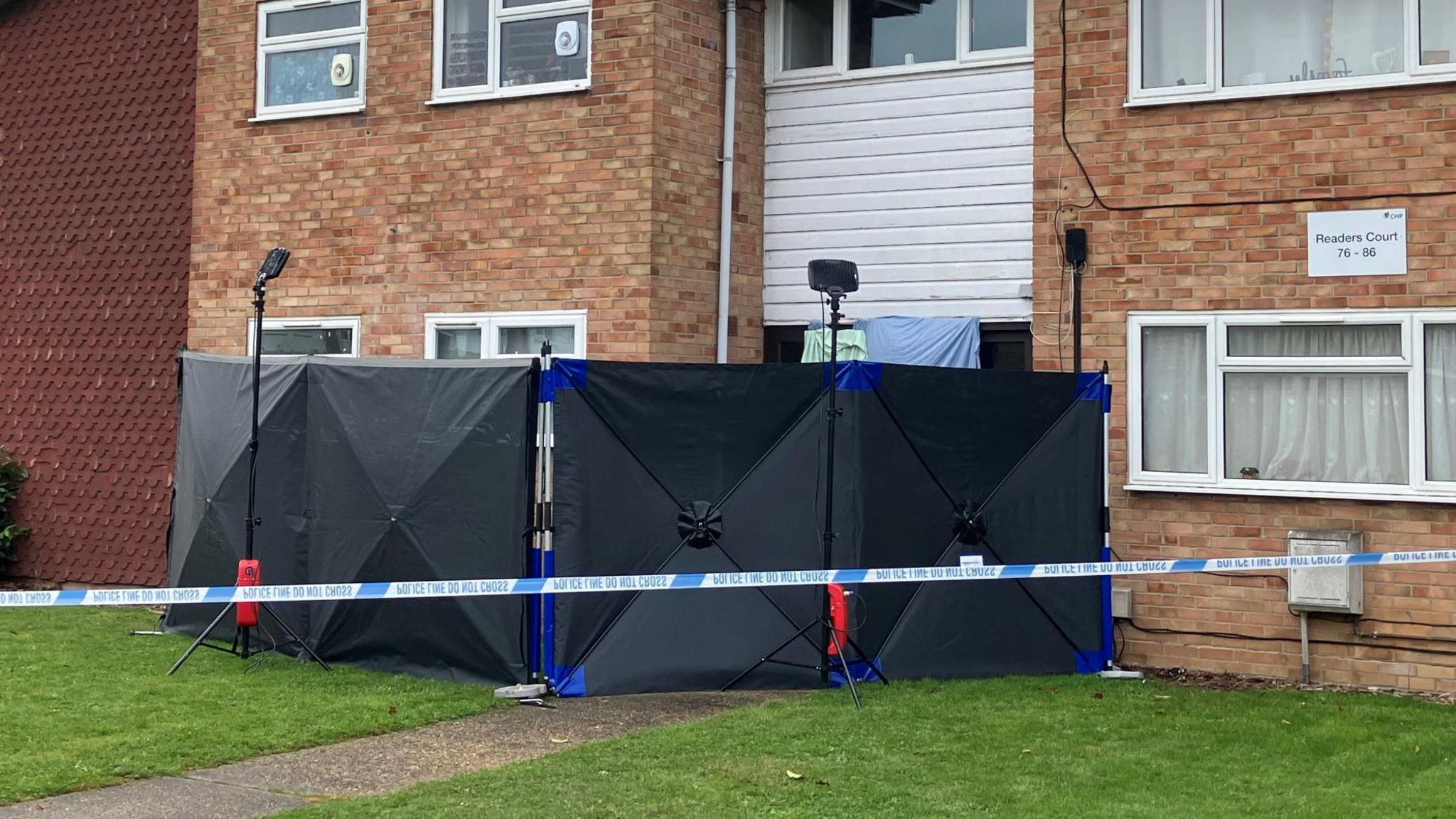 Black screens and police tape blocking off the entrance to a two-storey block of flats.