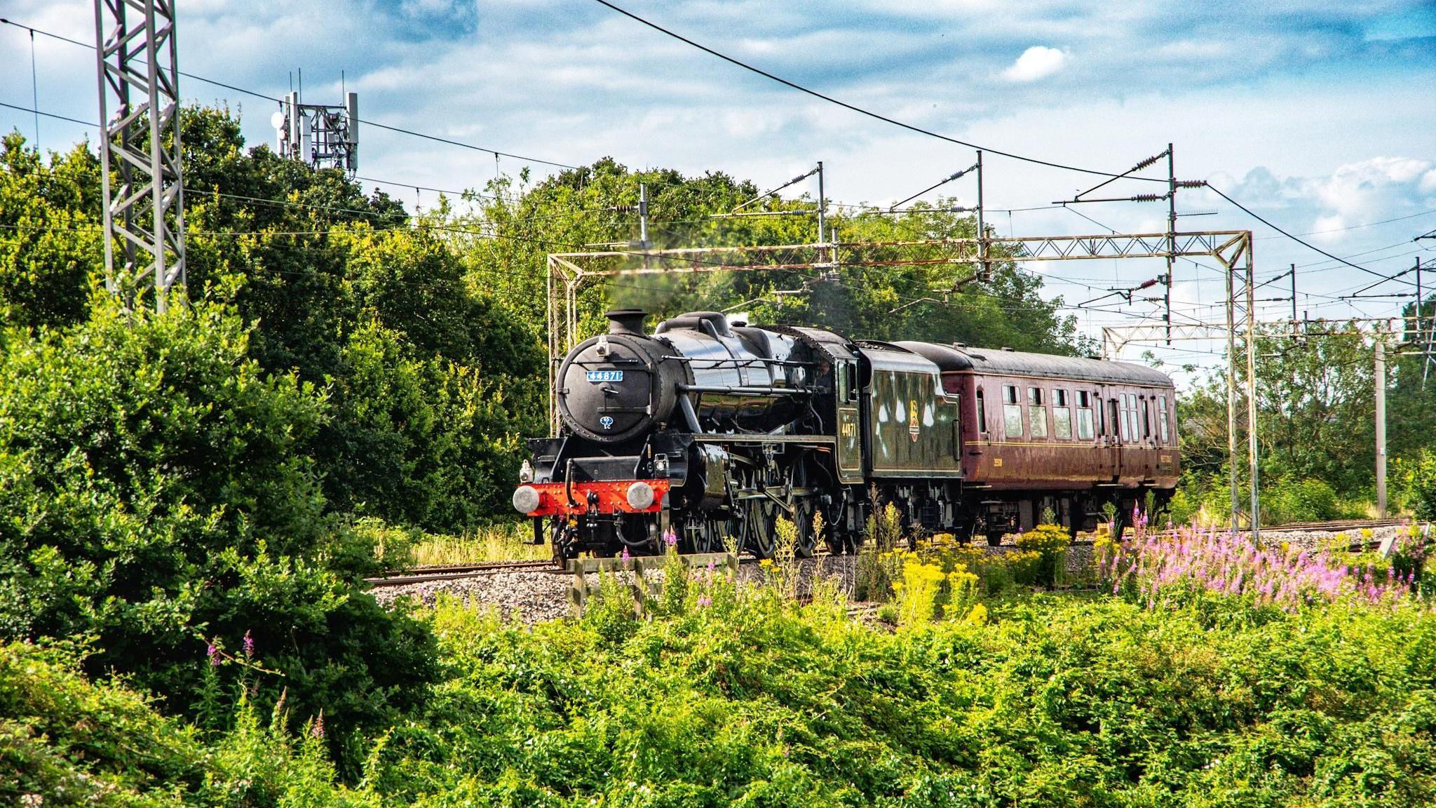 Steam train travelling through the countryside near Bulkington, Warwickshire. The train contrasts with modern power lines overhead