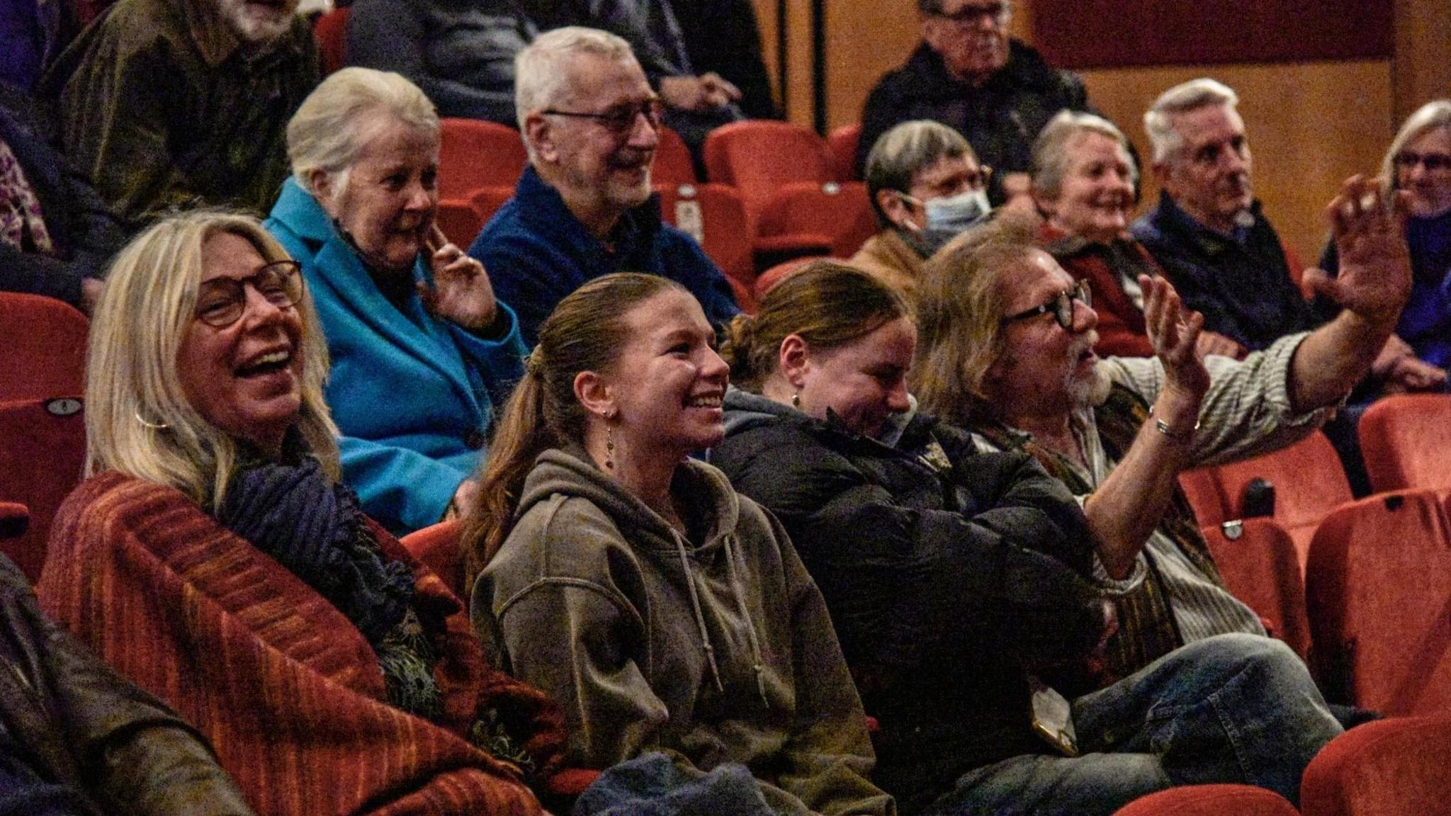 An audience is seated in cinema chairs, watching a film.