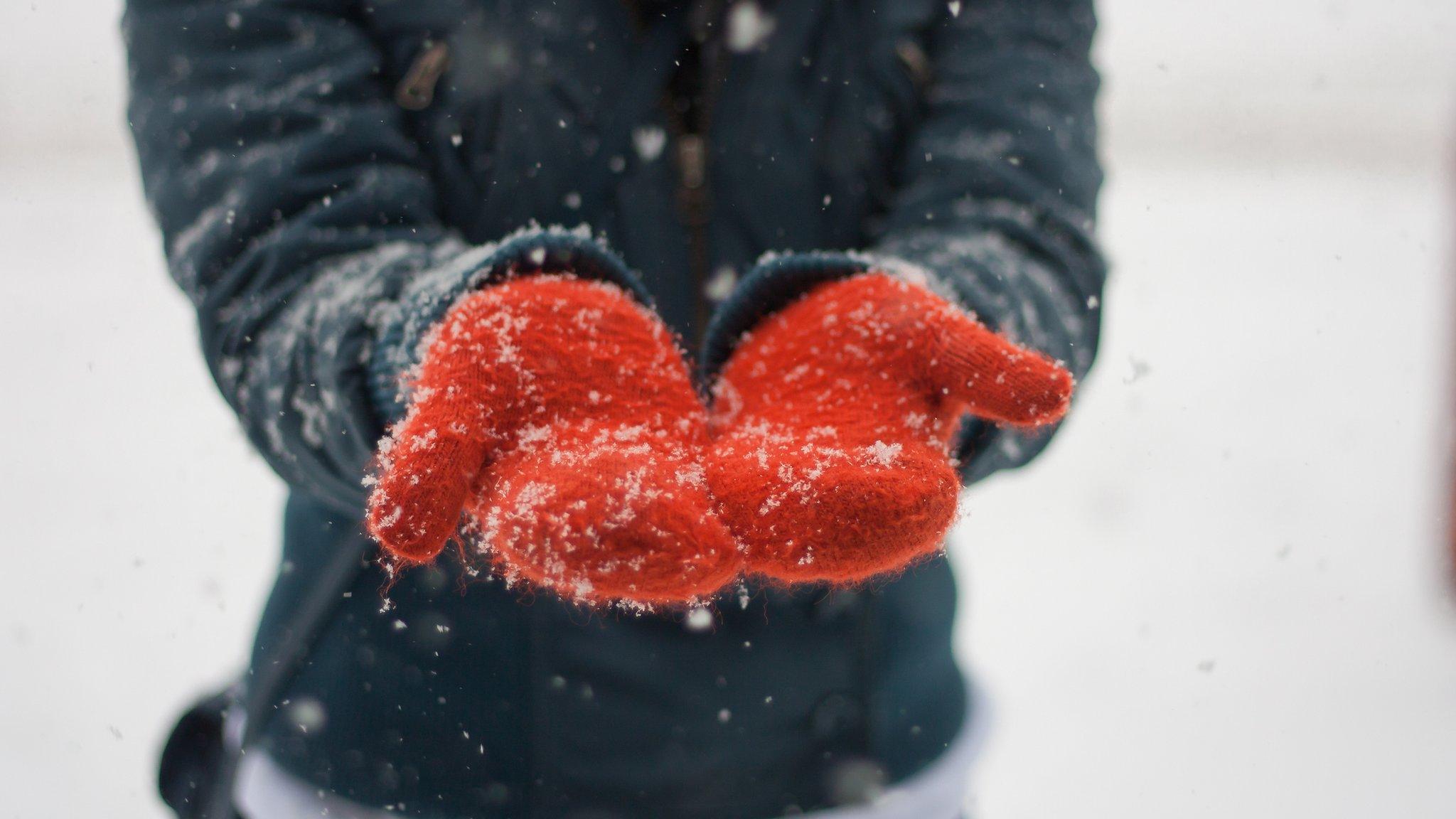 A woman wearing red gloves stands in the snow