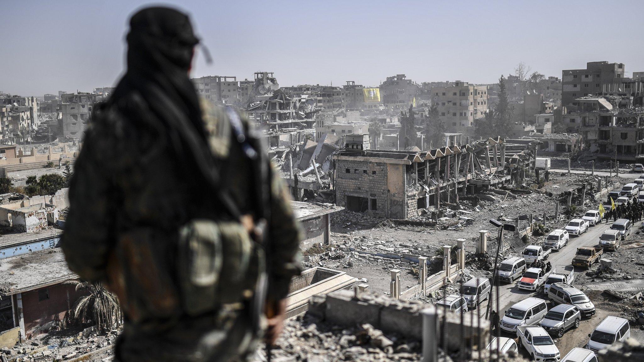 A fighter of the Syrian Democratic Forces stands guard on a rooftop in Raqqa after retaking the city from Islamic State