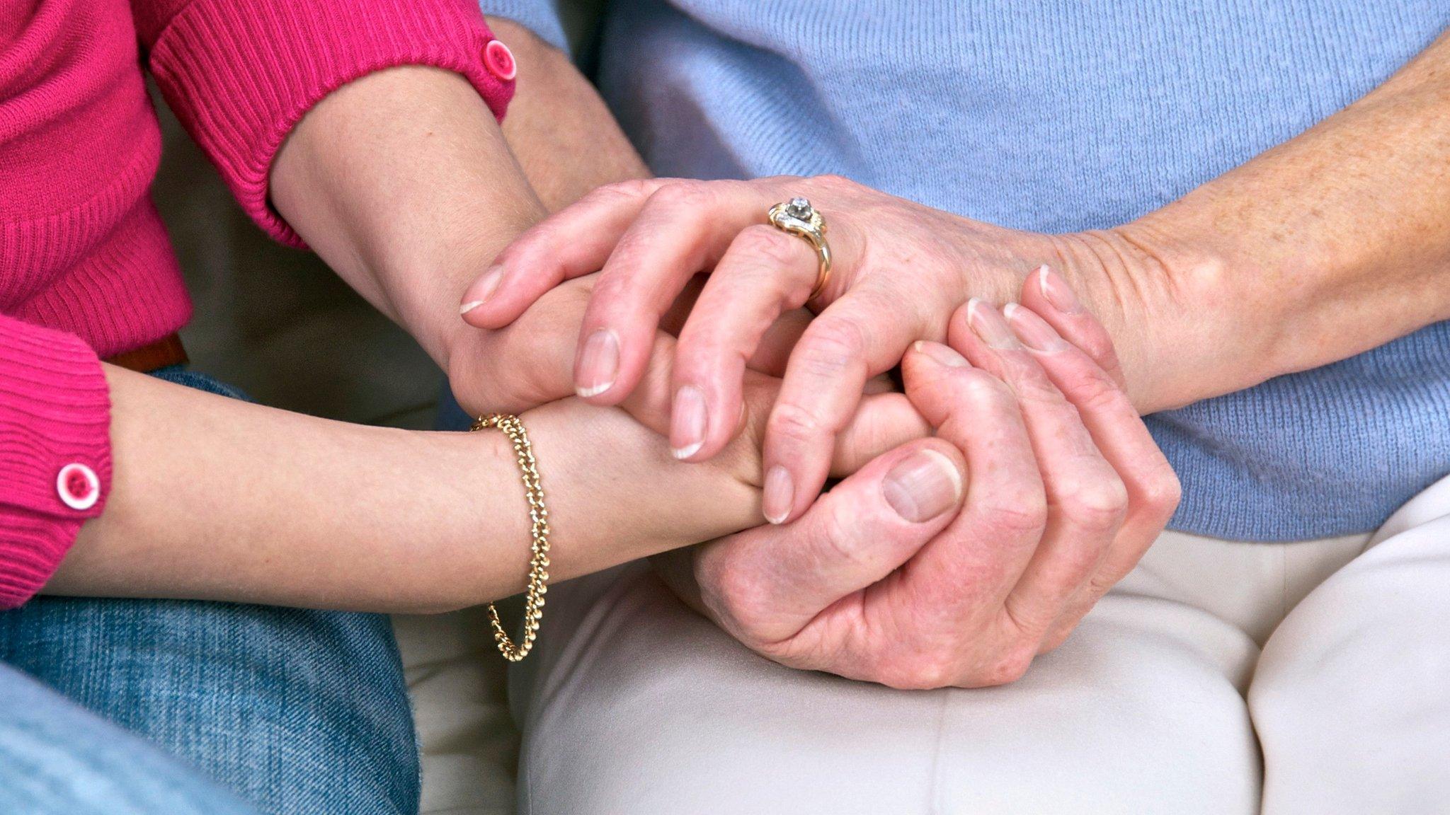 Elderly woman being comforted by a young woman holding her hands.