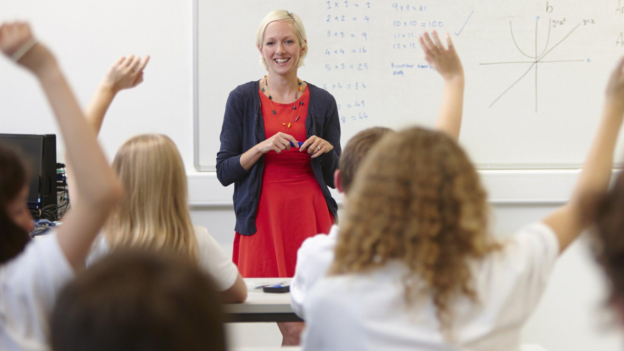 Female teacher and class with hands raised - stock photo