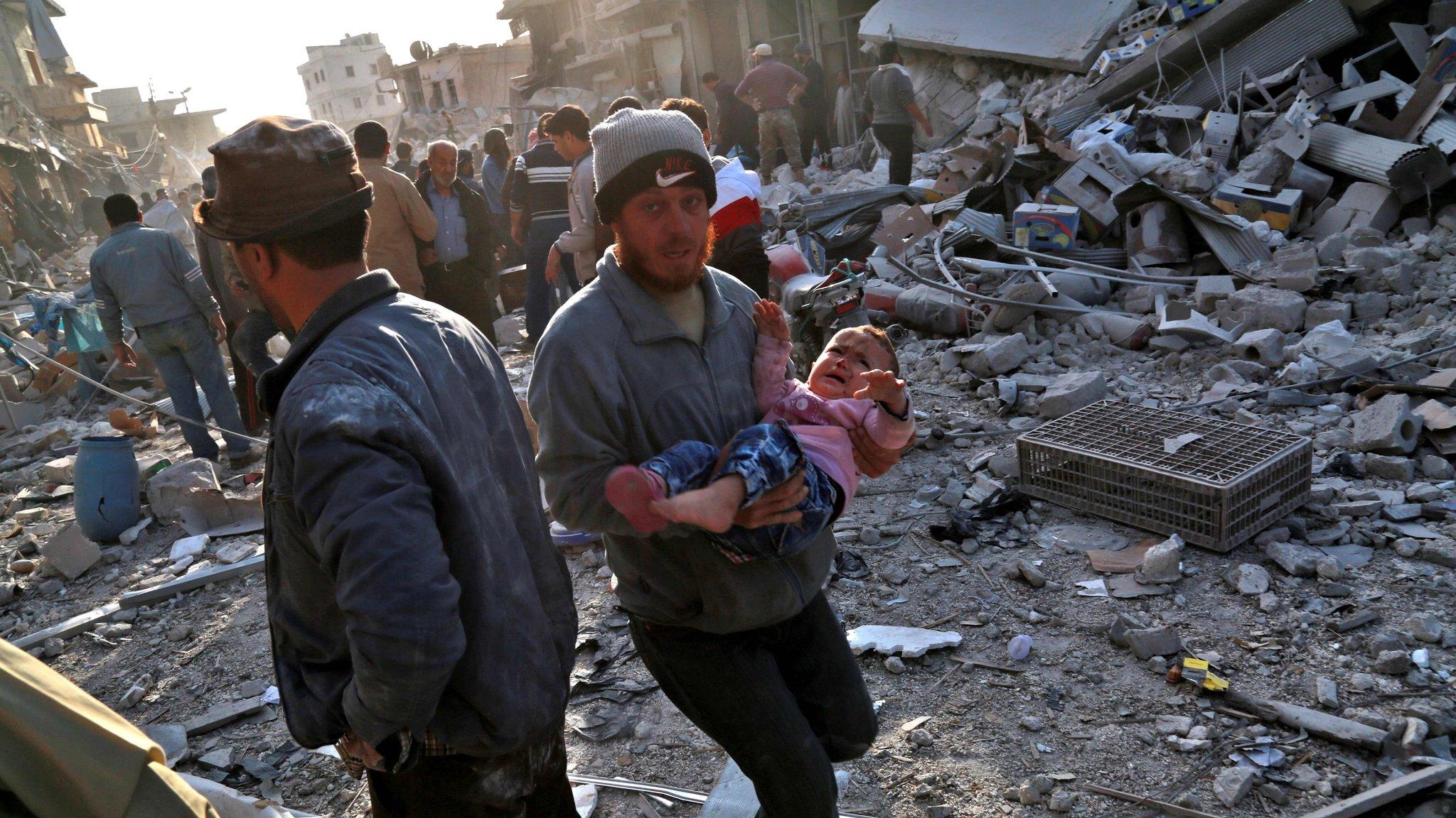 A Syrian man carries a child following a reported air strike on the rebel-held town of Atareb in northern Syria on 13 November 2017