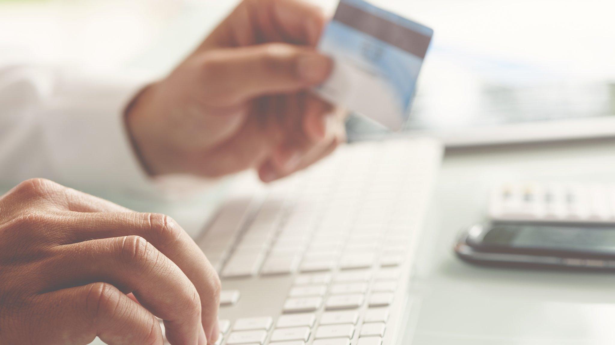 Man holds a credit card while typing on a computer keyboard