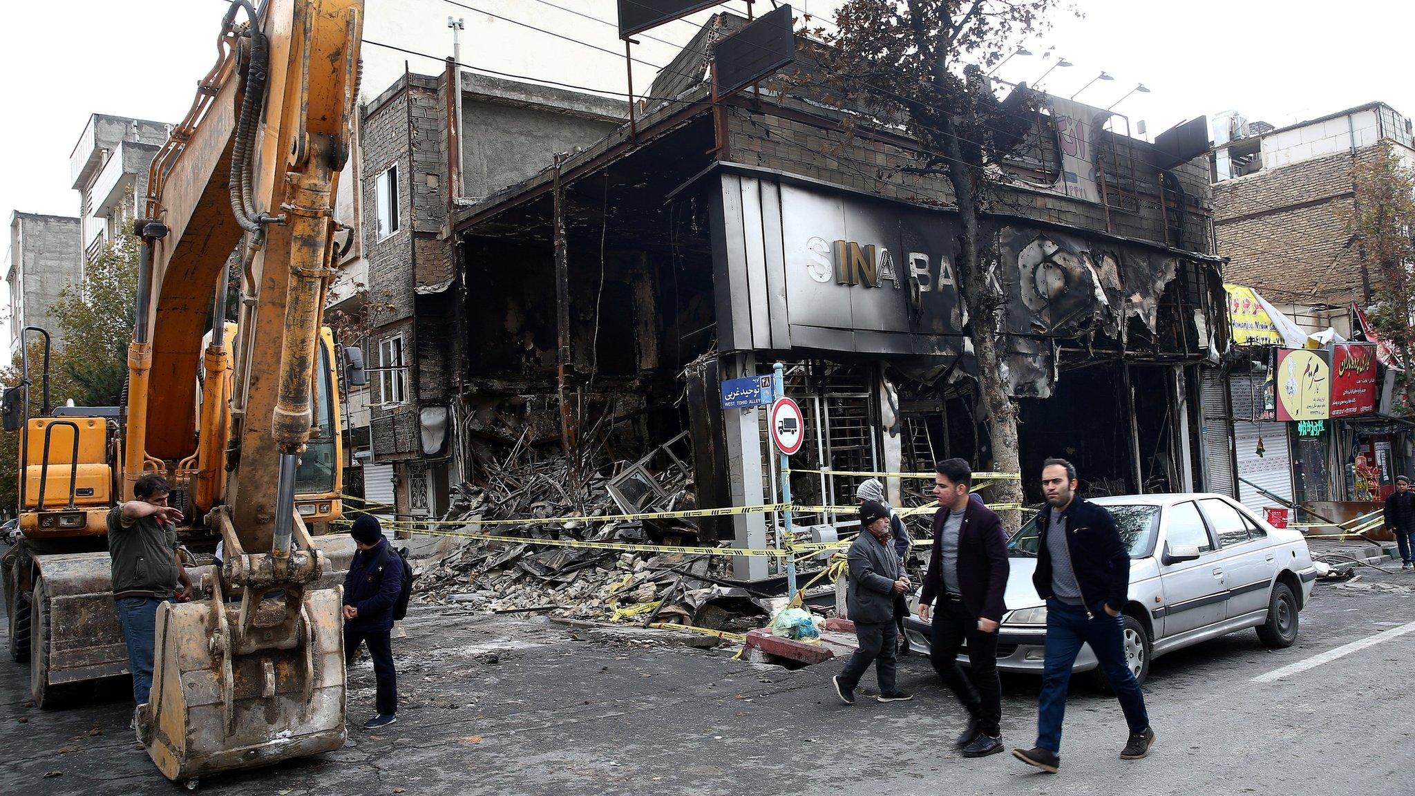 File photo showing people walking past a burned bank in Tehran, Iran (20 November 2019)