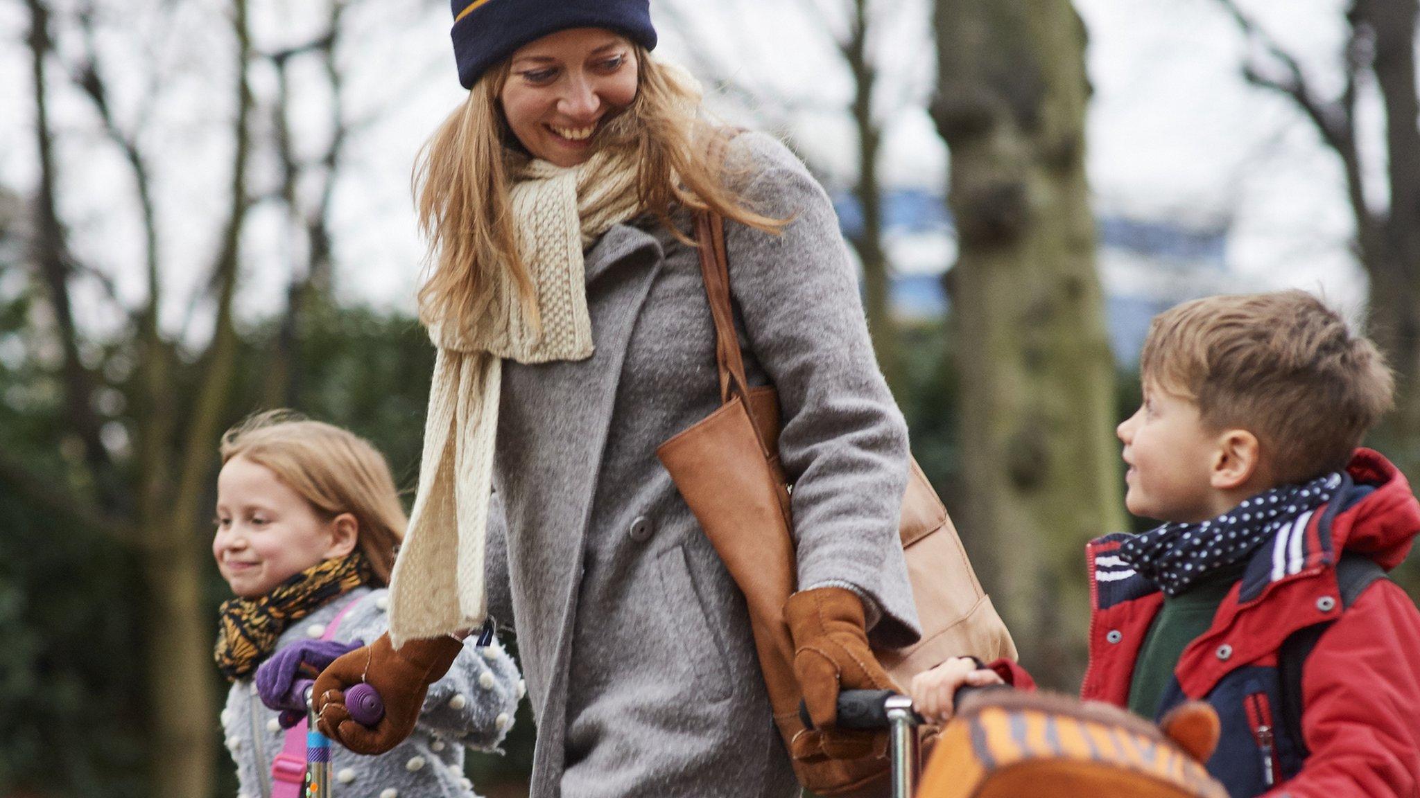 Young mum walking her children from school with their scooters, on cold autumn afternoon (stock photo)