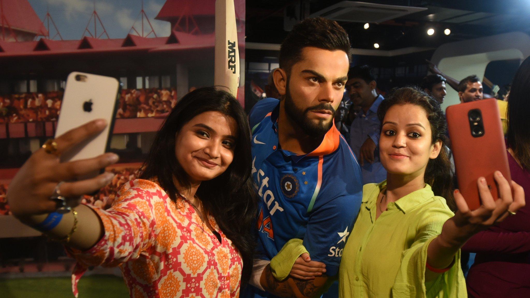 Delhi, India, 6 June: Two girls take selfies with the newly installed wax statue of cricketer Virat Kohli, at a museum in the iconic Regal Building, in the Indian capital. (Photo by Sushil Kumar/ Hindustan Times via Getty Images)