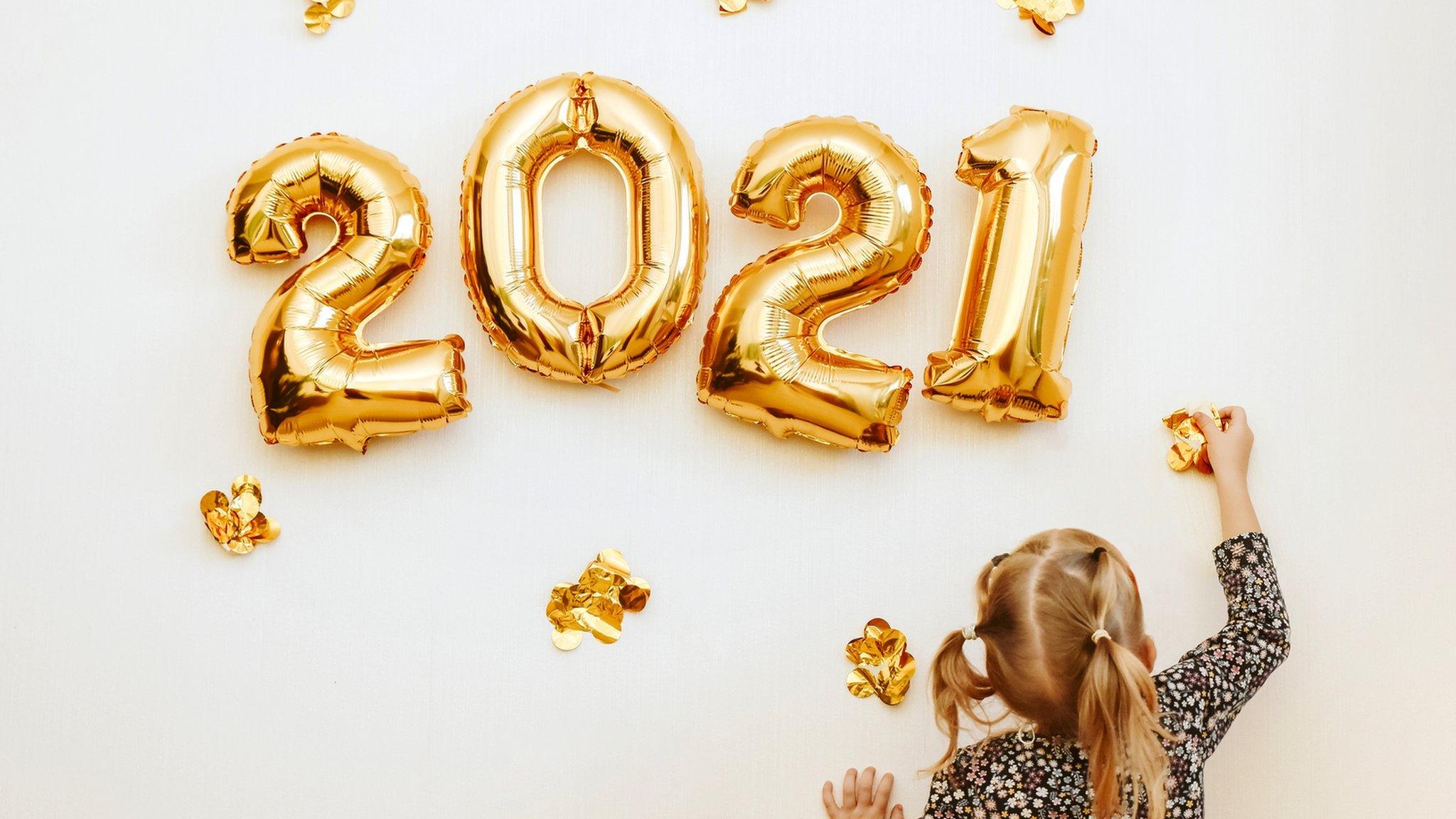 A girl reaches up to balloons spelling out 2021