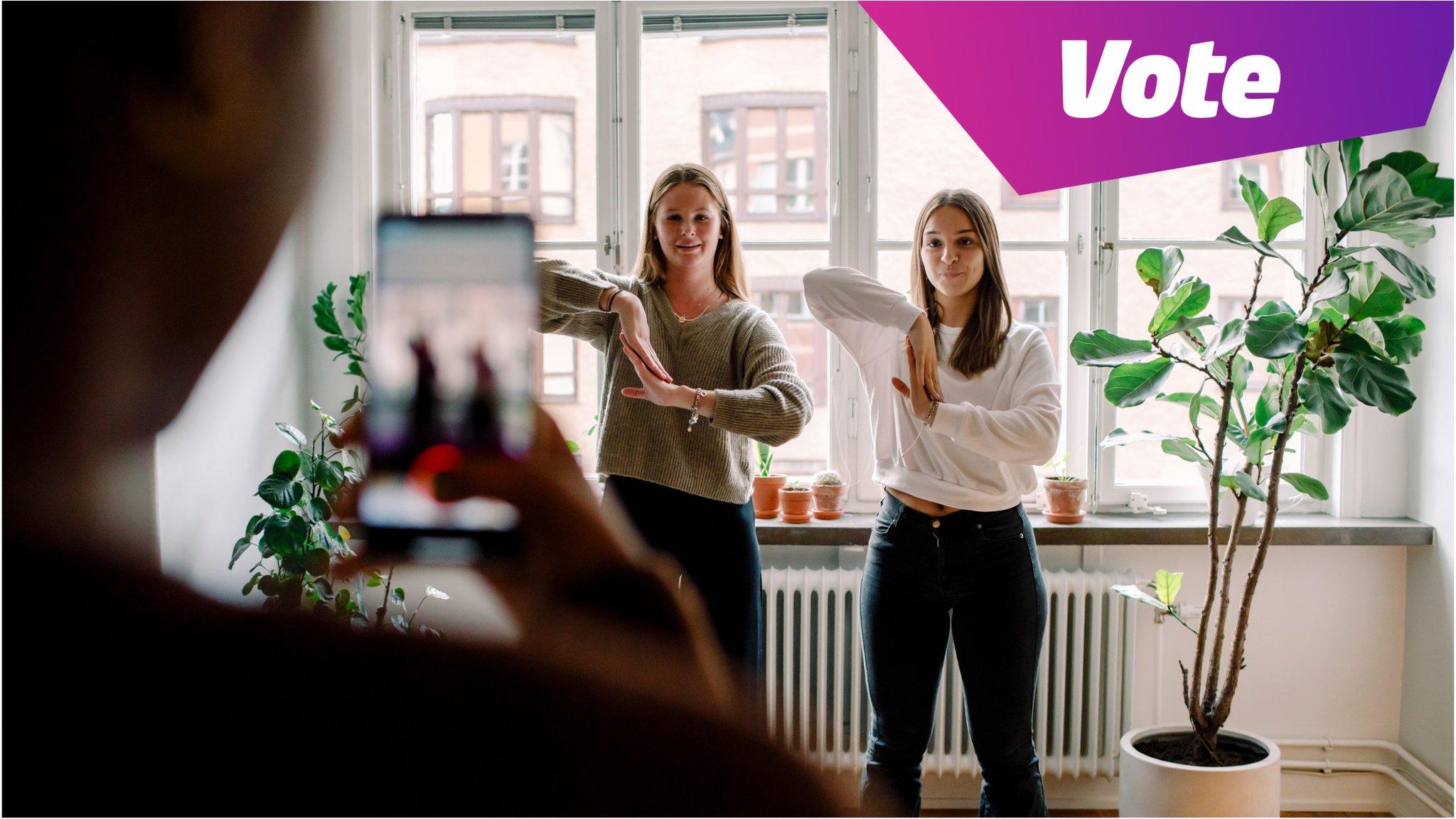 Two girls dancing and being filmed on a phone.