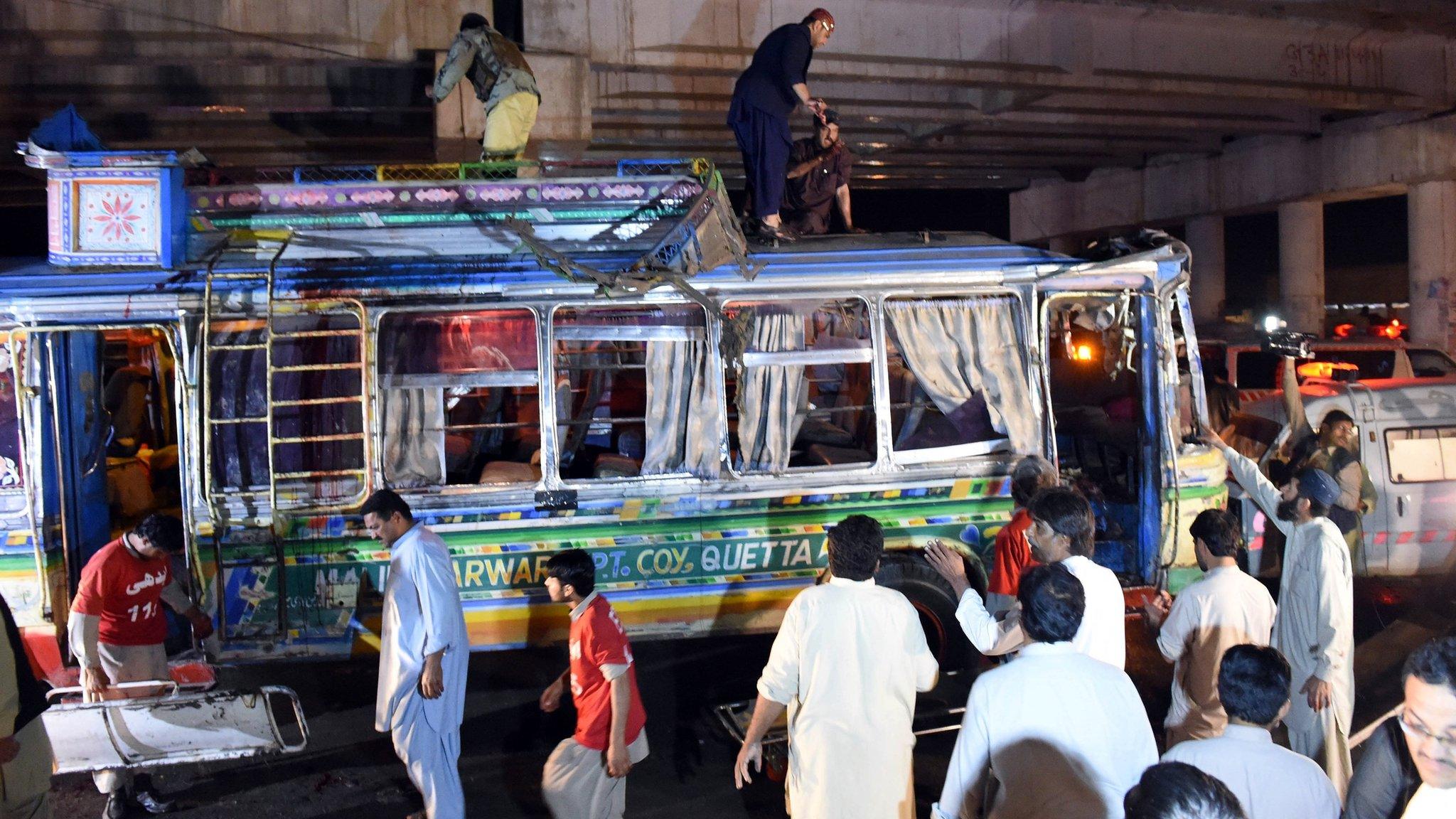 Pakistani volunteers and residents gather beside a damaged bus after a bomb explosion in Quetta on October 19, 2015