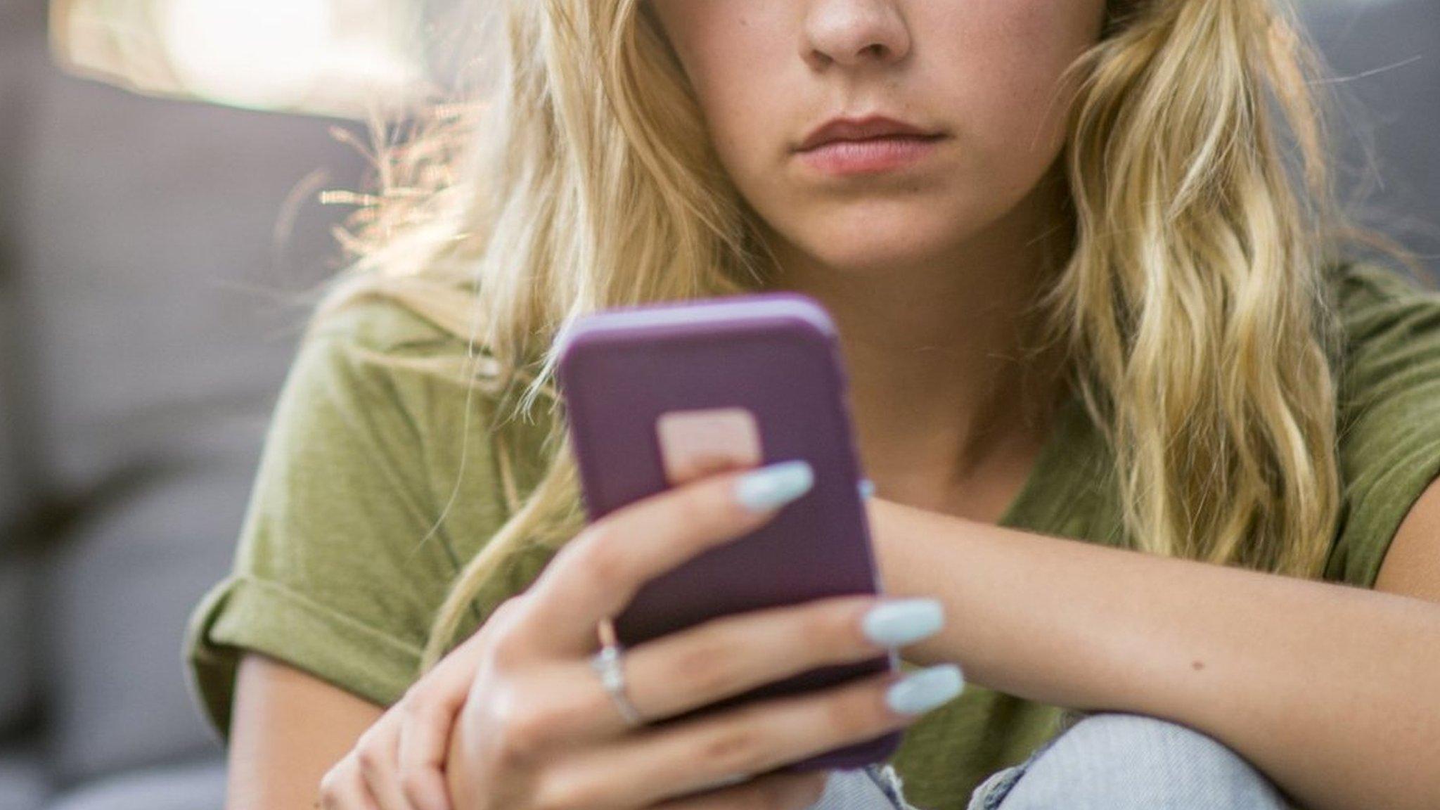 A girl looking solemnly at her smartphone.