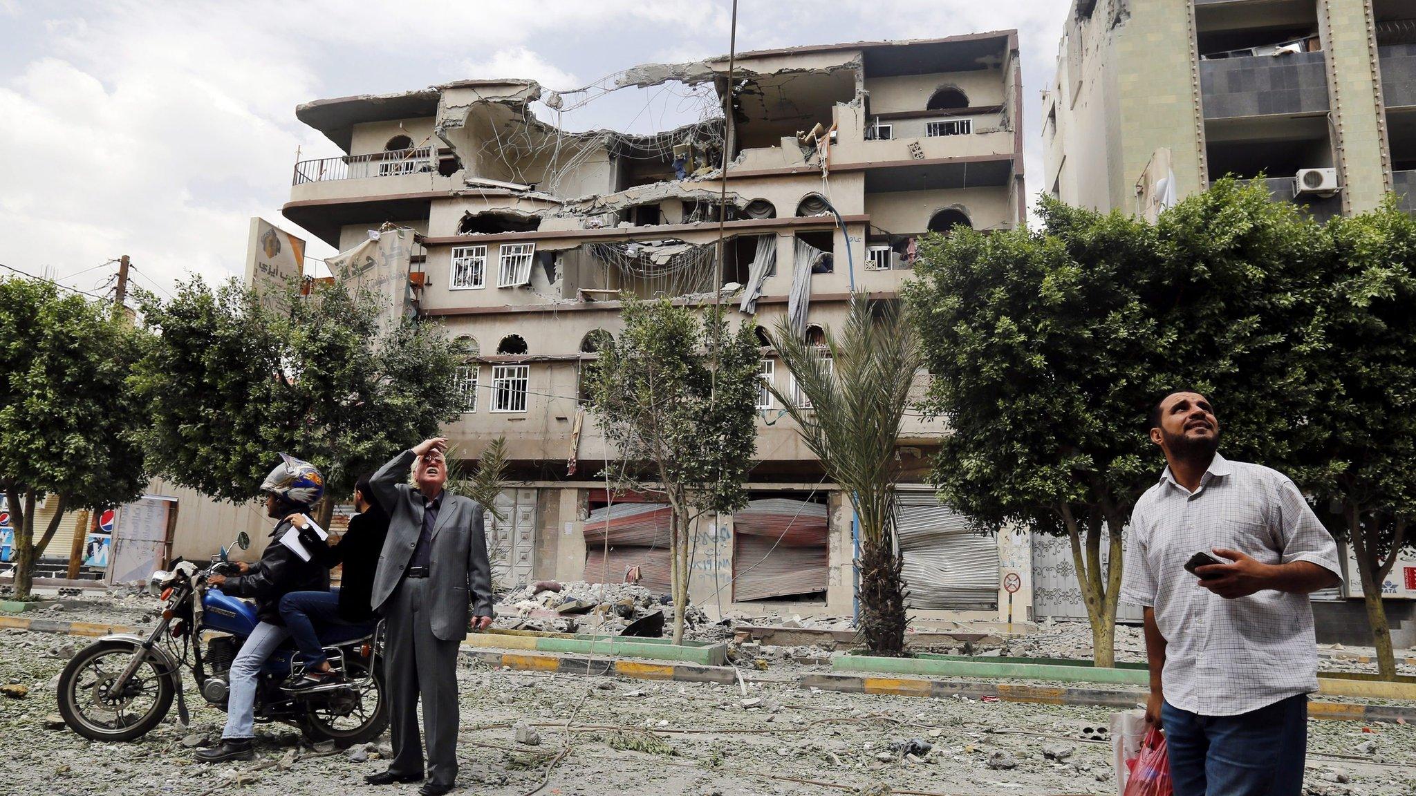 Yemenis stop and look up in front of a building heavily damaged in Saudi-led coalition airstrikes