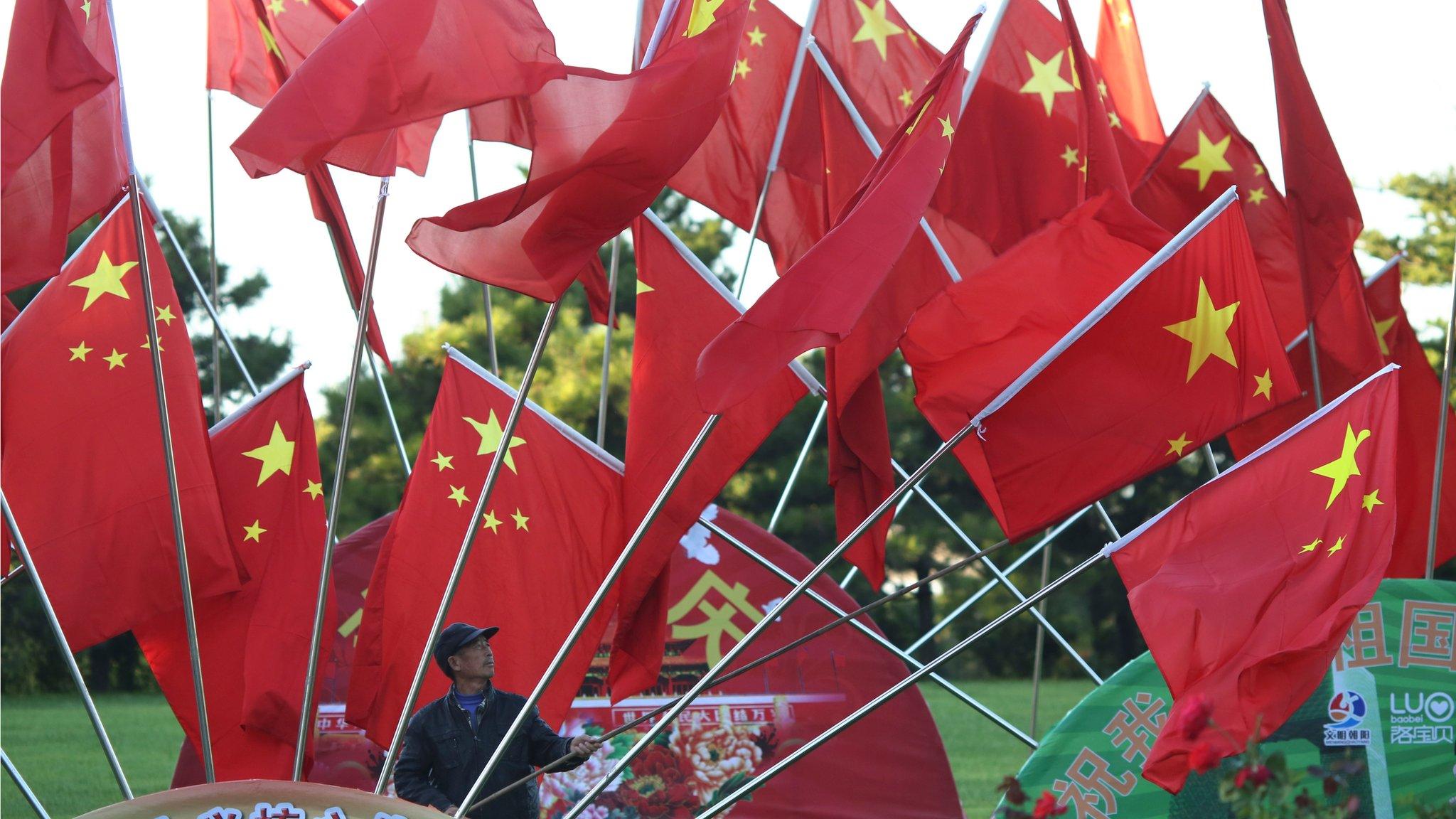 A worker adjusts a Chinese national flag displayed for the country's national day at a park in Beijing