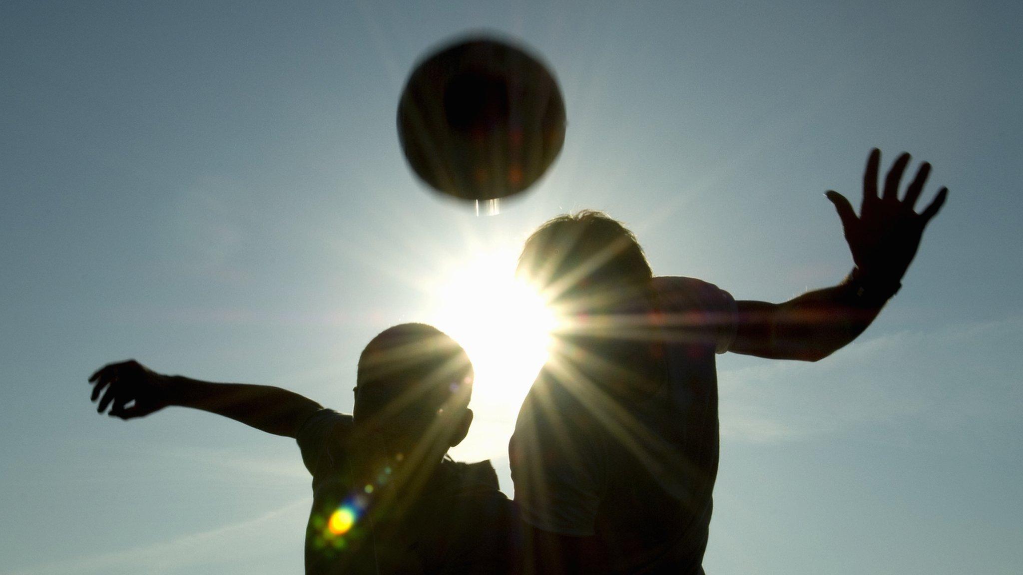 Two silhouetted footballers heading the ball