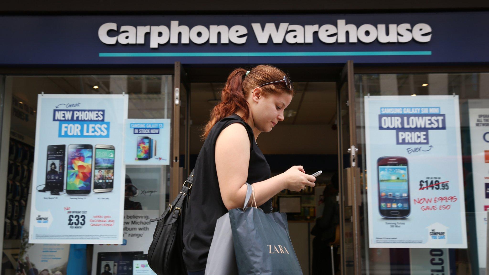 A woman walks past a Carphone Warehouse store texting on a mobile phone