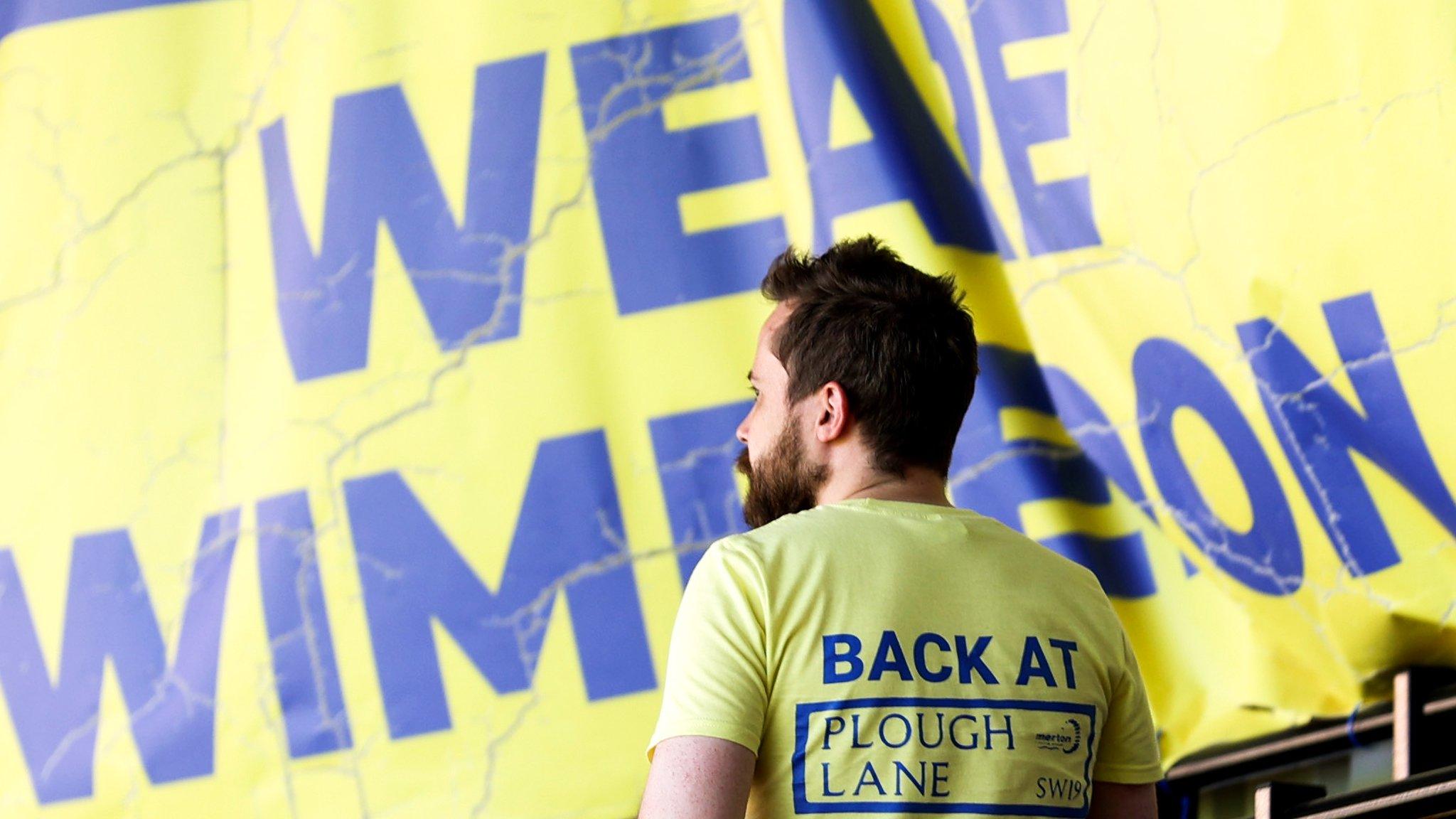 An AFC Wimbledon fan wearing a T-Shirt reading: Back at Plough Lane