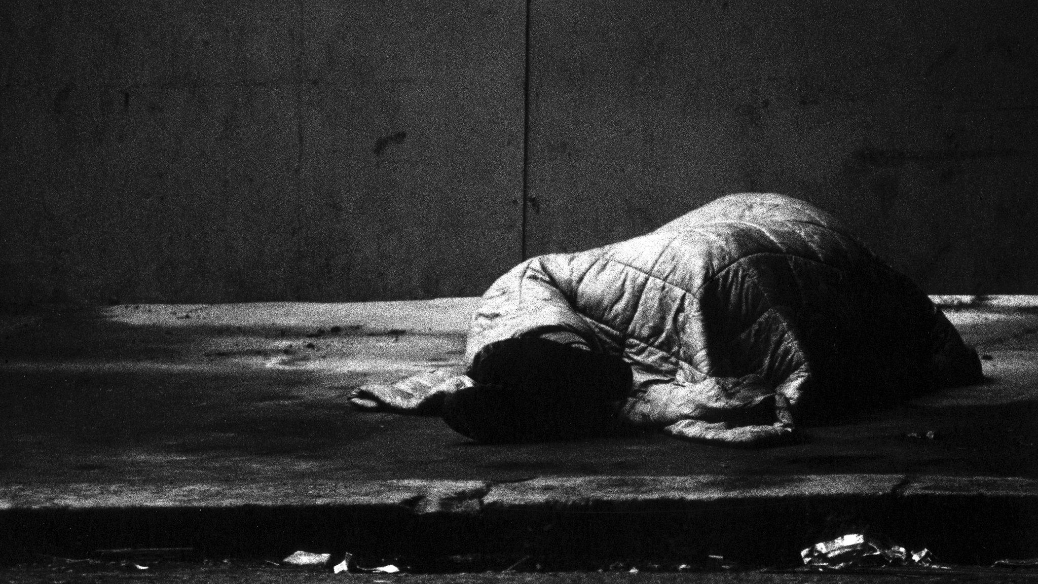 Sleeping rough - a person hidden by a sleeping bag on the street in a black and white image