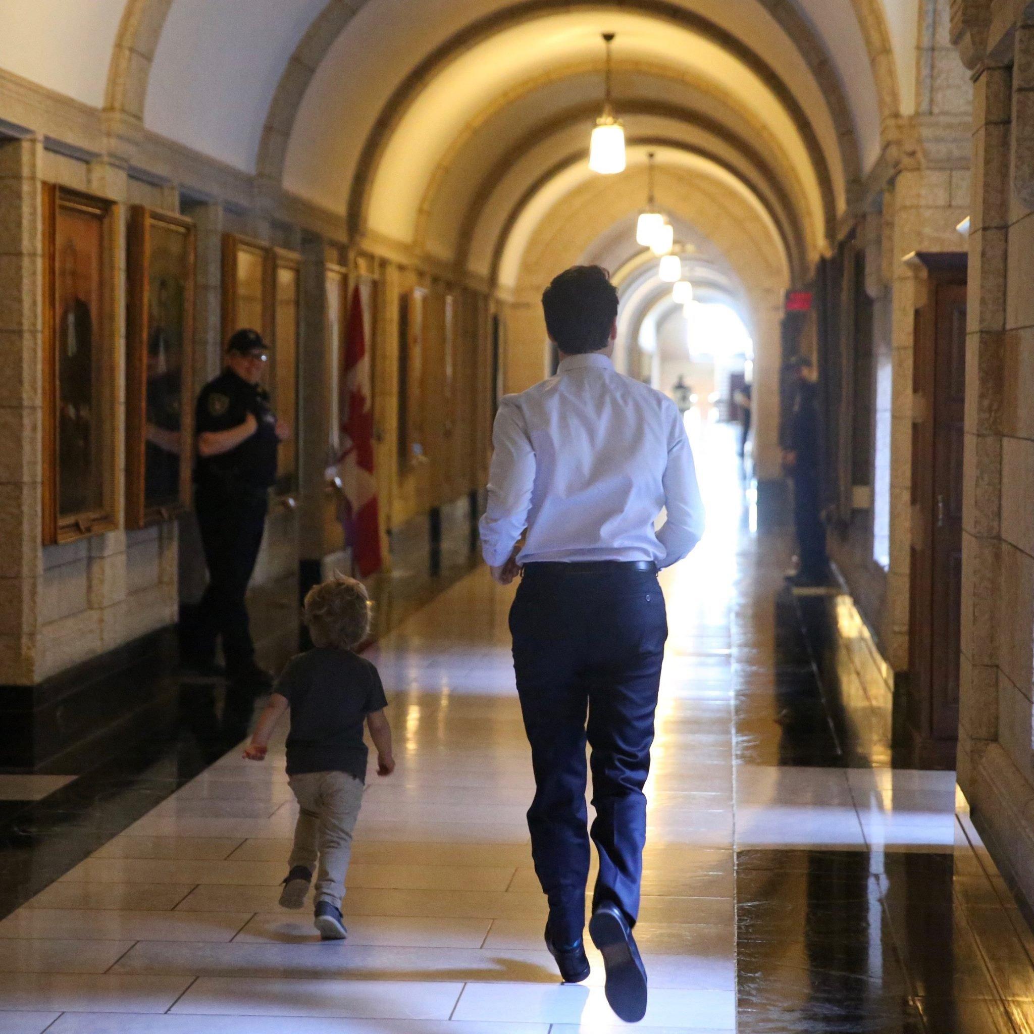 Photographed from behind, Justin Trudeau and his three-year-old son run down an expensive-looking government building while smiling security guards look on