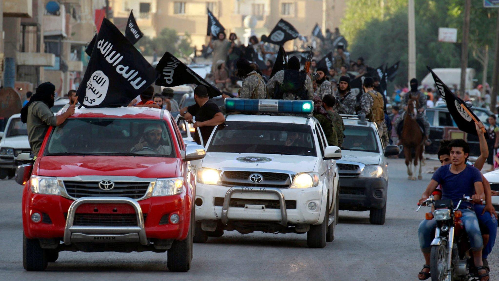 IS militant hold up black jihadist banners in Raqqa on 30 June 2014