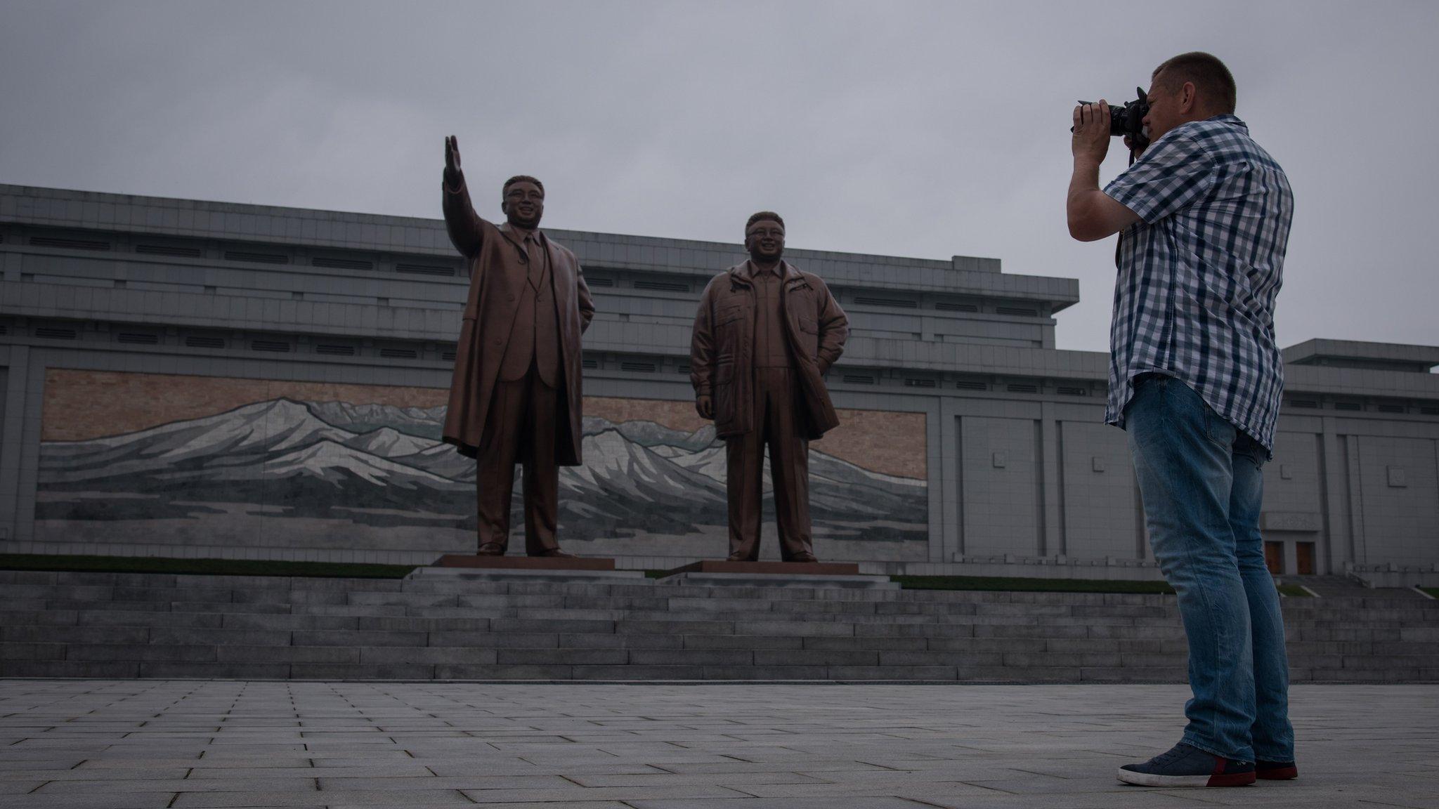 A tourist takes a photo of statues of late North Korean leaders Kim Il-Sung (L) and Kim Jong-Il (R), on Mansu hill in Pyongyang on July 23, 2017