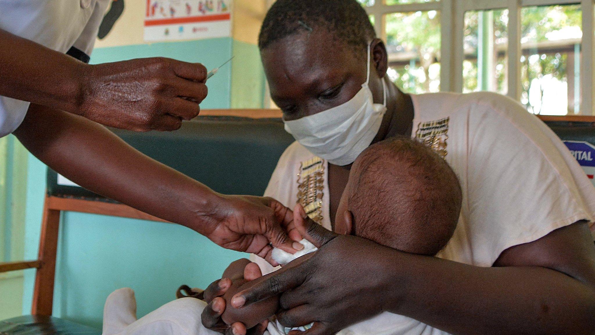 a baby receives a vaccine from malaria while being held by an adult