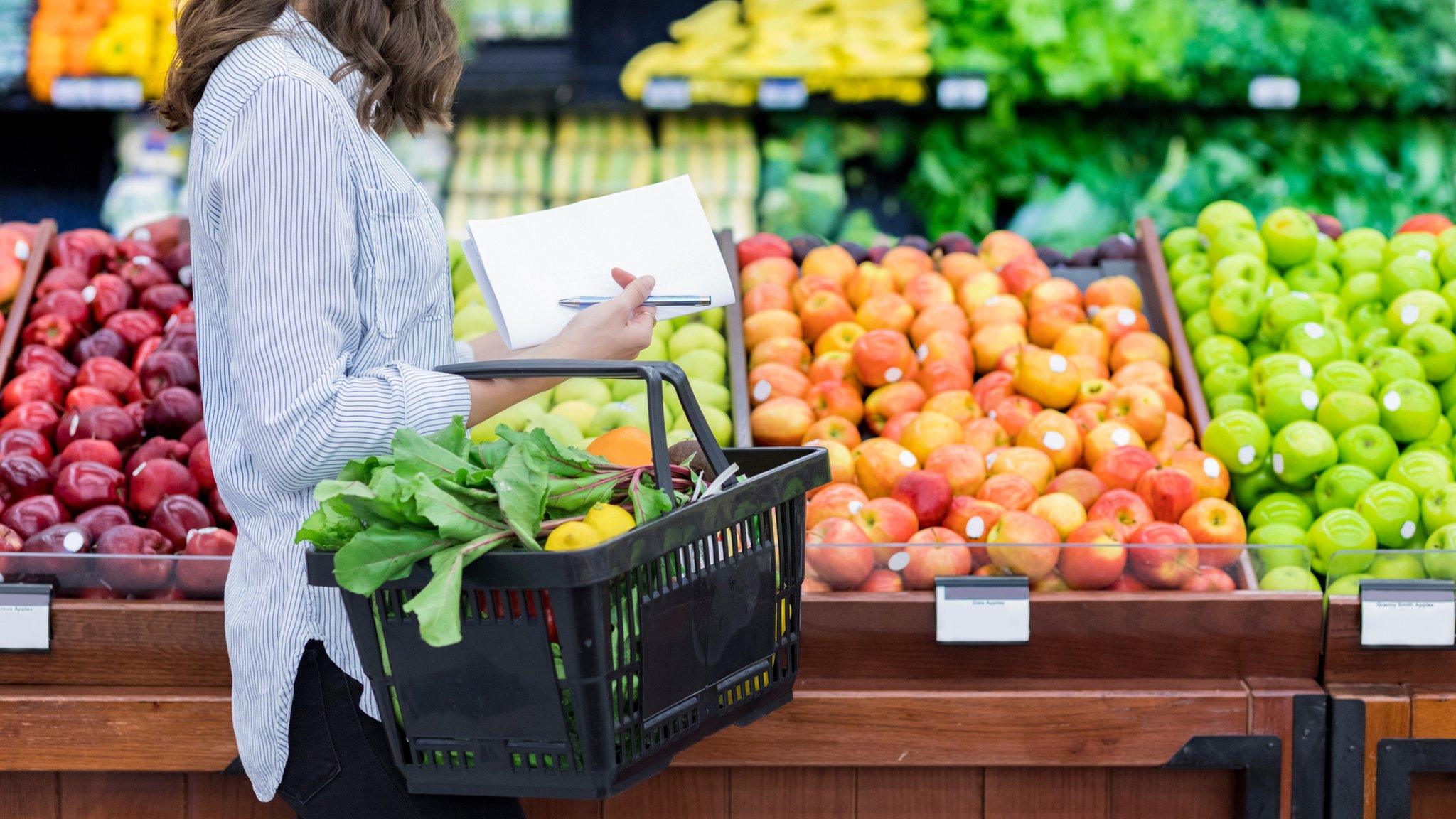 Woman carrying a basket of food in a supermarket fresh food section