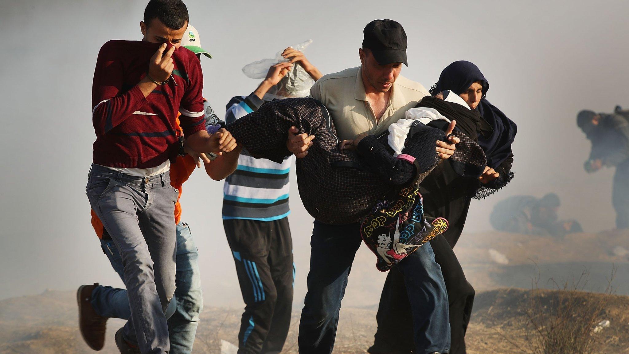 Palestinians run through tear gas carrying an injured woman during protests on the Gaza-Israel border on 15 May 2018