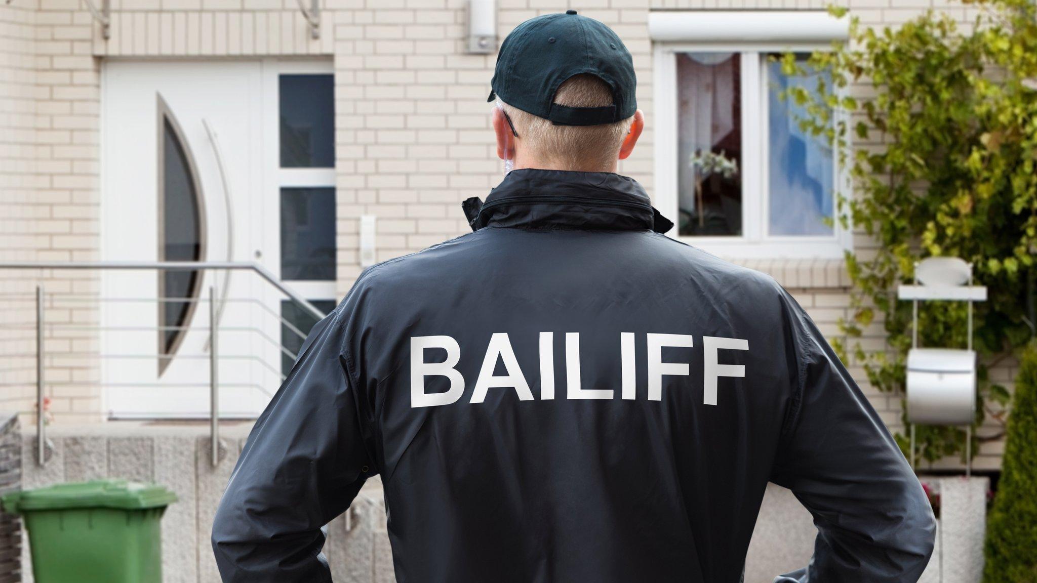 Bailiff stands in front of house