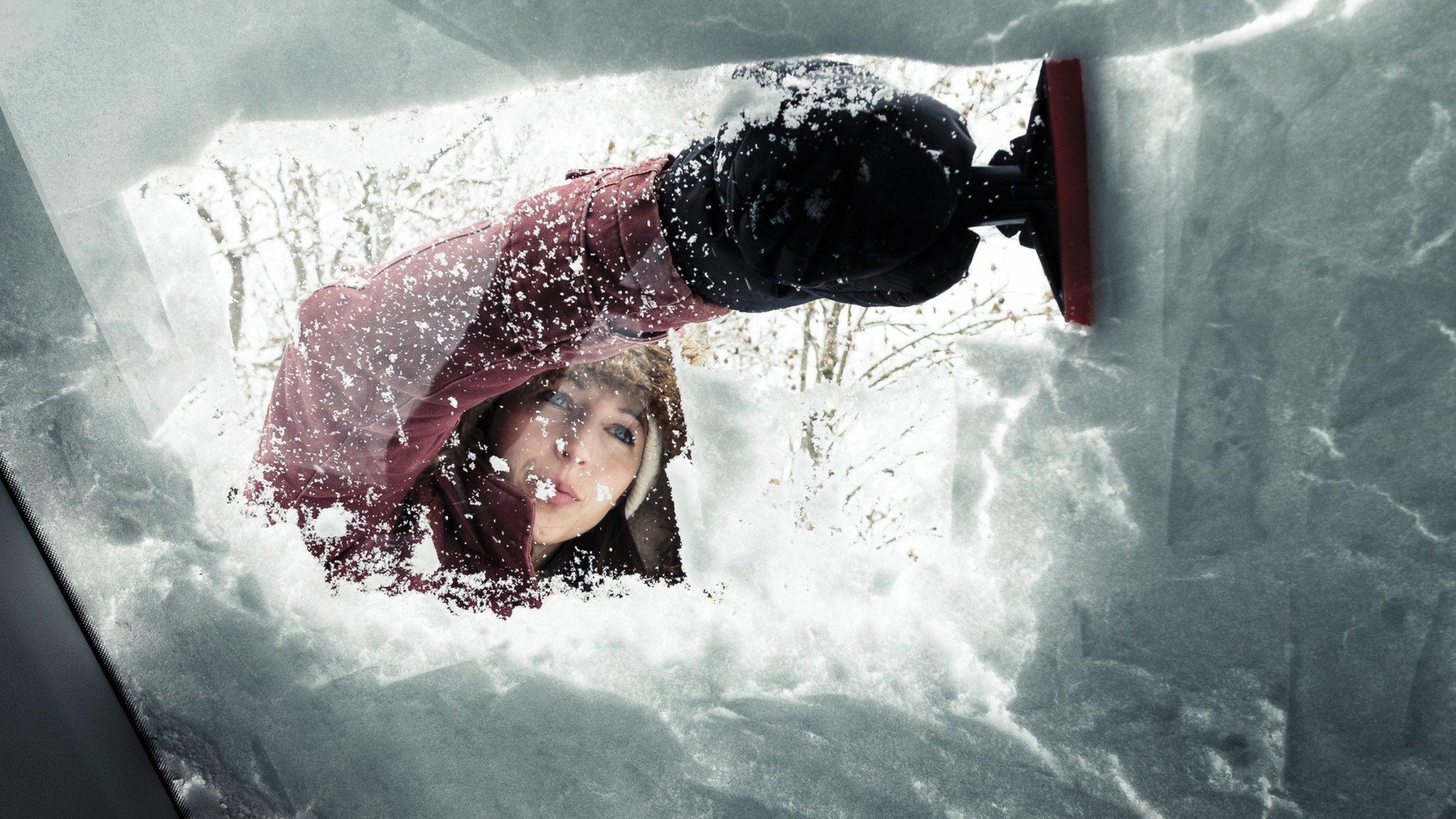 Portrait of young woman cleaning snow from car's windscreen - stock photo